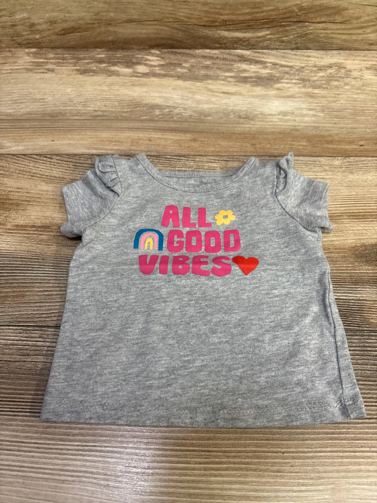Front view of gray Okie Dokie baby shirt in size 3 months showcasing All Good Vibes graphic with rainbow and heart on wood background