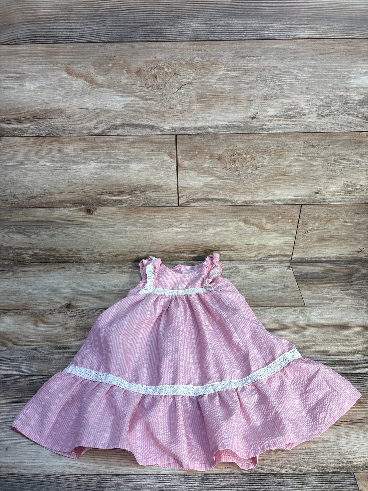 Front view of the pink RZ by Rachel Zoe lace trim dress showcasing ruffled shoulders and white lace bands on a wood background