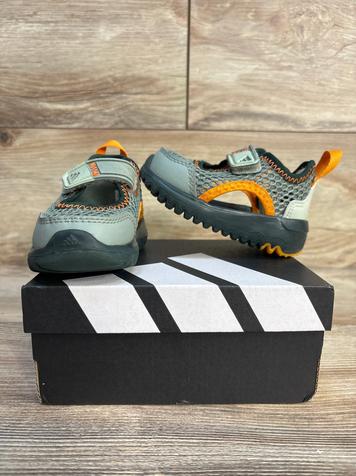 Kids' gray and orange water shoes with hook-and-loop straps on a shoebox, wood background