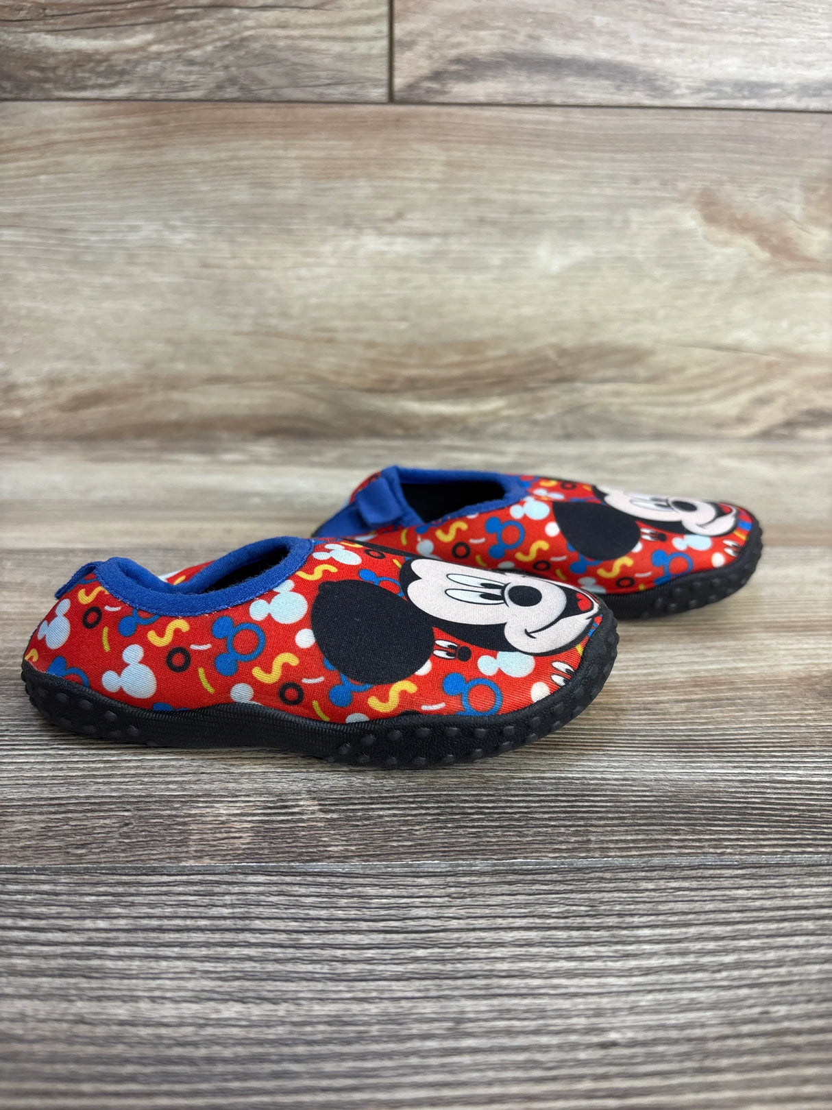 Side view of Disney Baby Mickey Mouse Water Shoes sz 7/8c showcasing red shoes with Mickey print and blue trim on wood plank floor