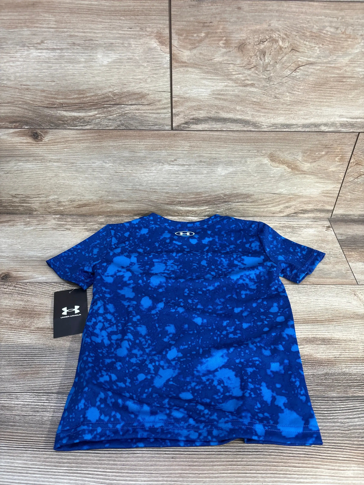 Front view of NEW Under Armour Active Shirt Blue sz 4T showcasing blue splatter pattern, crewneck, and short sleeves on a wood background