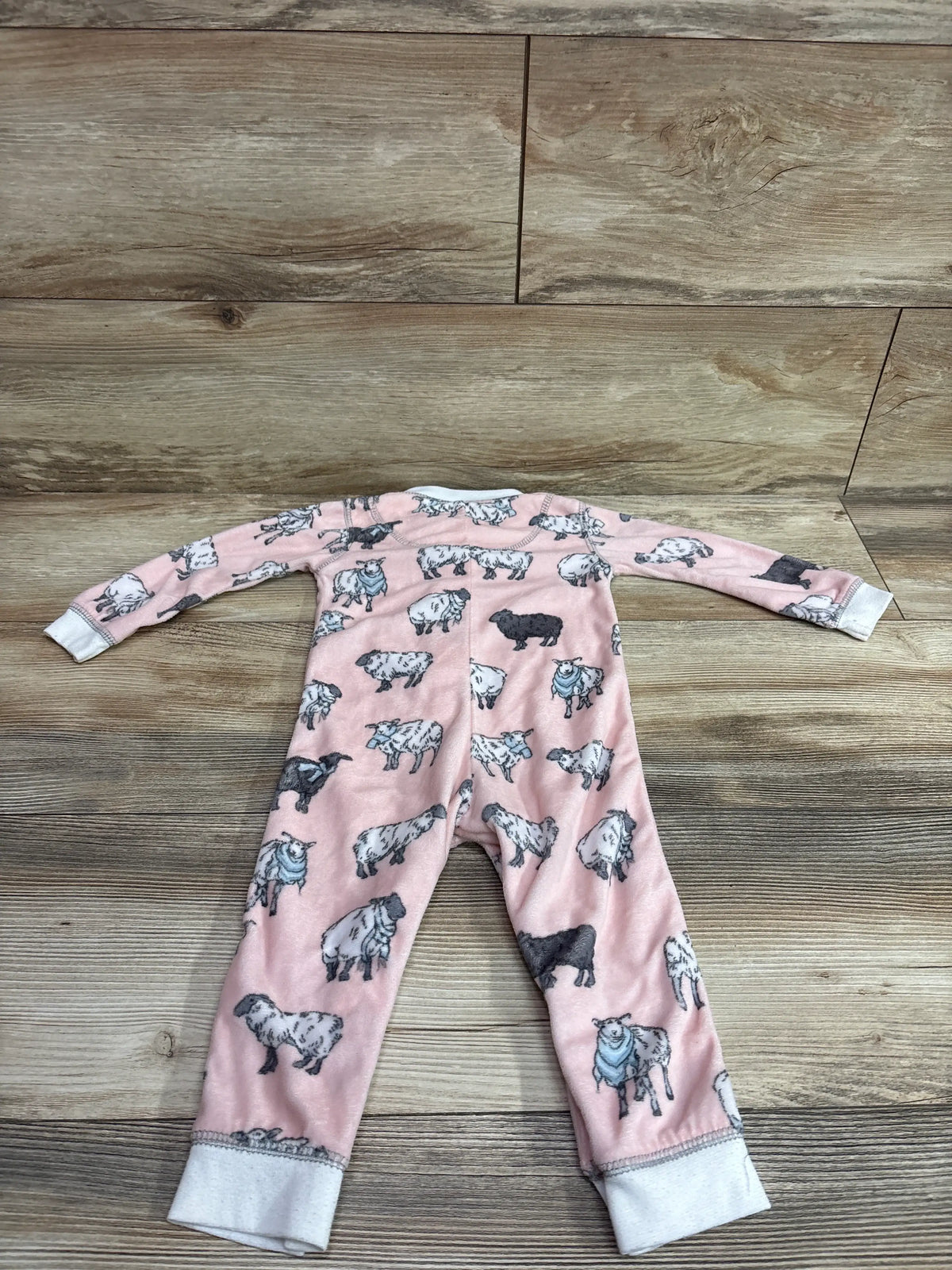 Front view of a pink PJ Salvage blanket sleeper for ages 12 to 18 months with a sheep print and gray cuffs on a wood floor