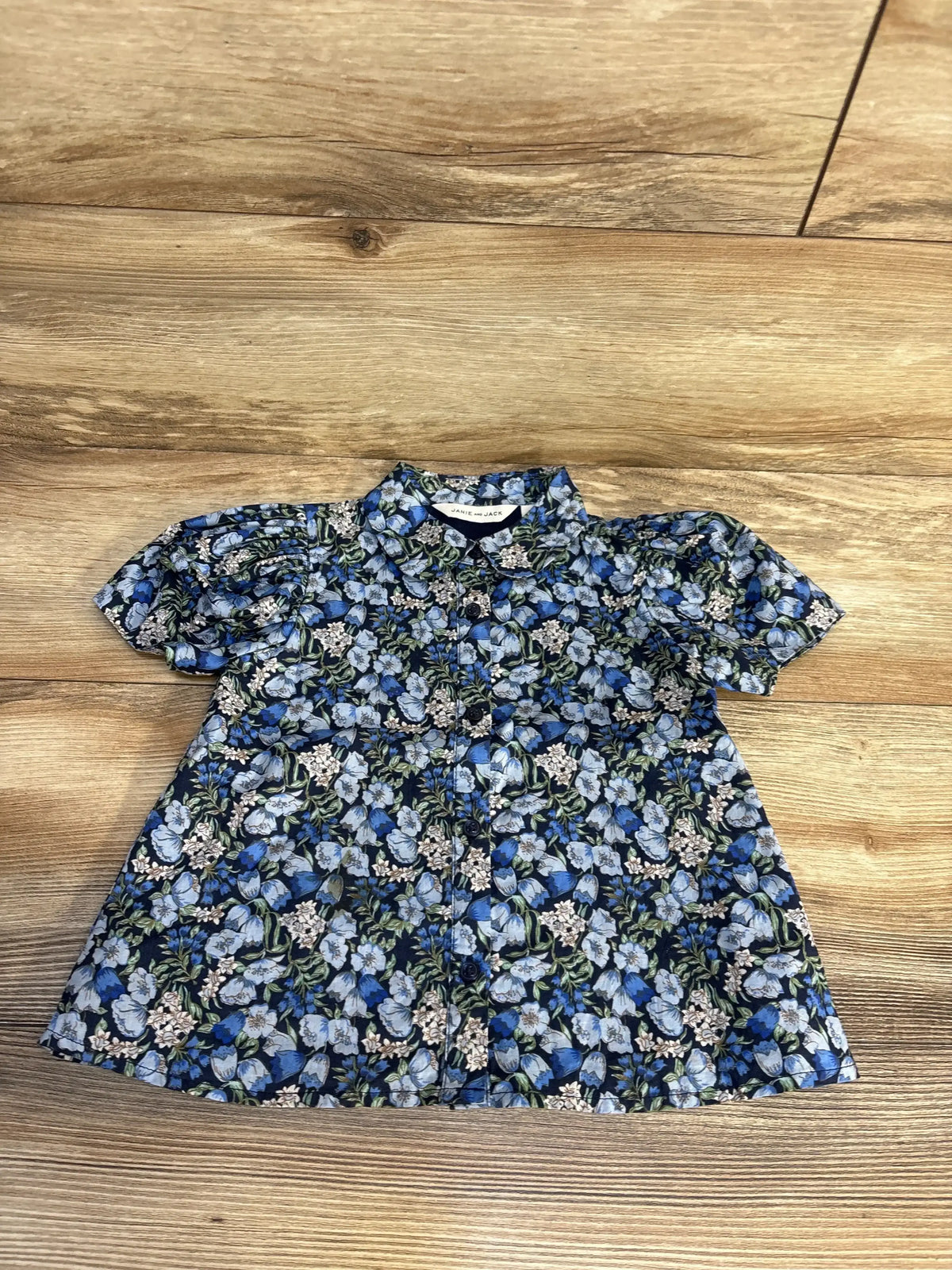 Top view of Janie and Jack floral button-up shirt in blue showcasing a collared short-sleeve design on a wood floor