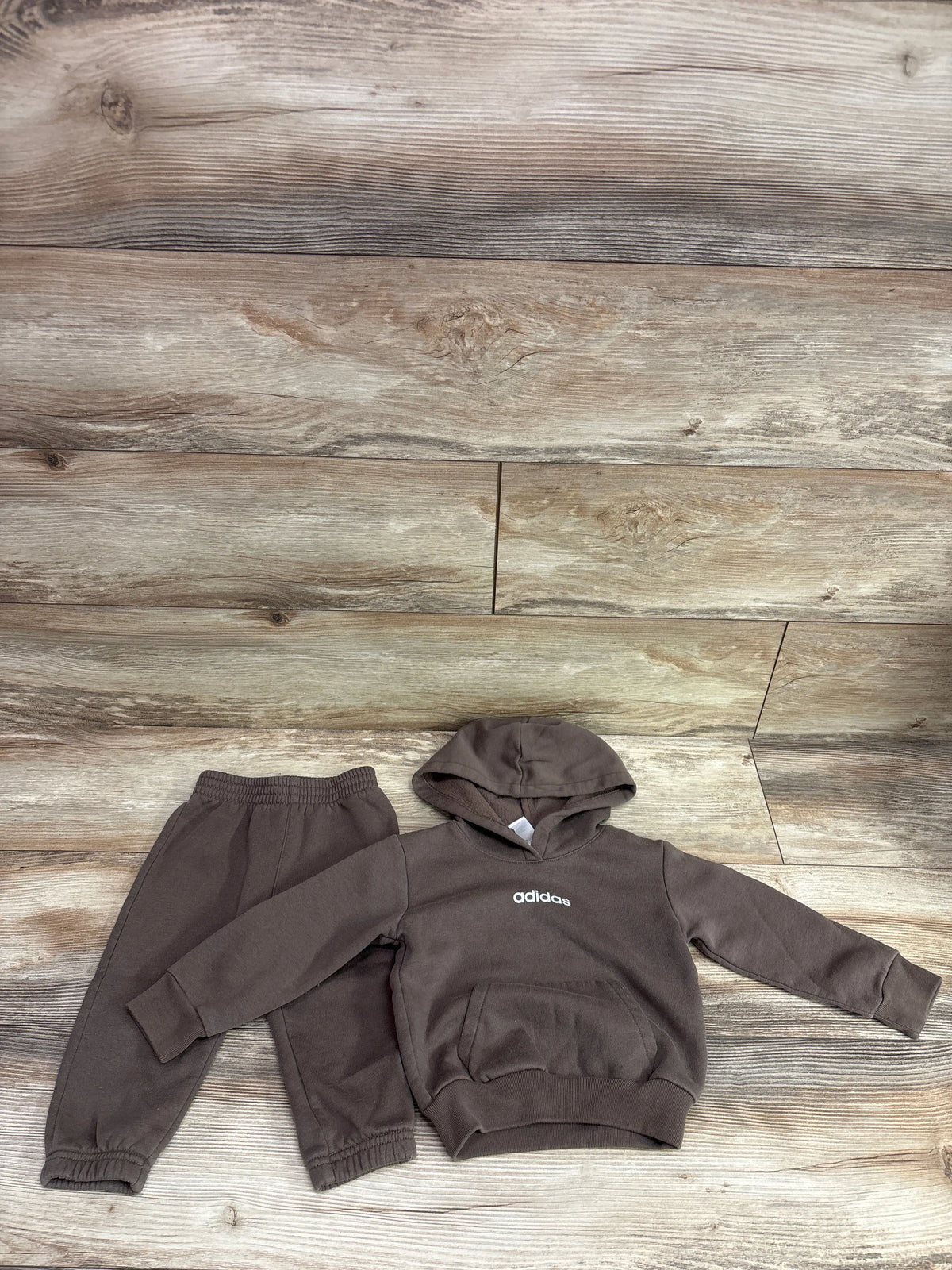 Overhead view of brown Adidas two-piece pullover sweatshirt and joggers set showcasing hood and elastic cuffs on wood planks