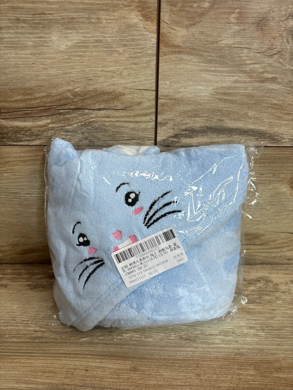 Front folded view of light blue bunny hooded baby bath towel showing embroidered bunny face and ears on wood background