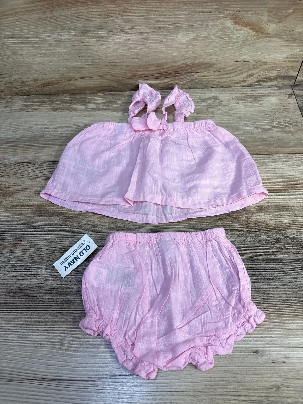 Flat lay Old Navy pink baby tank and bloomers showing ruffled shoulder ties and elastic waist on wood background