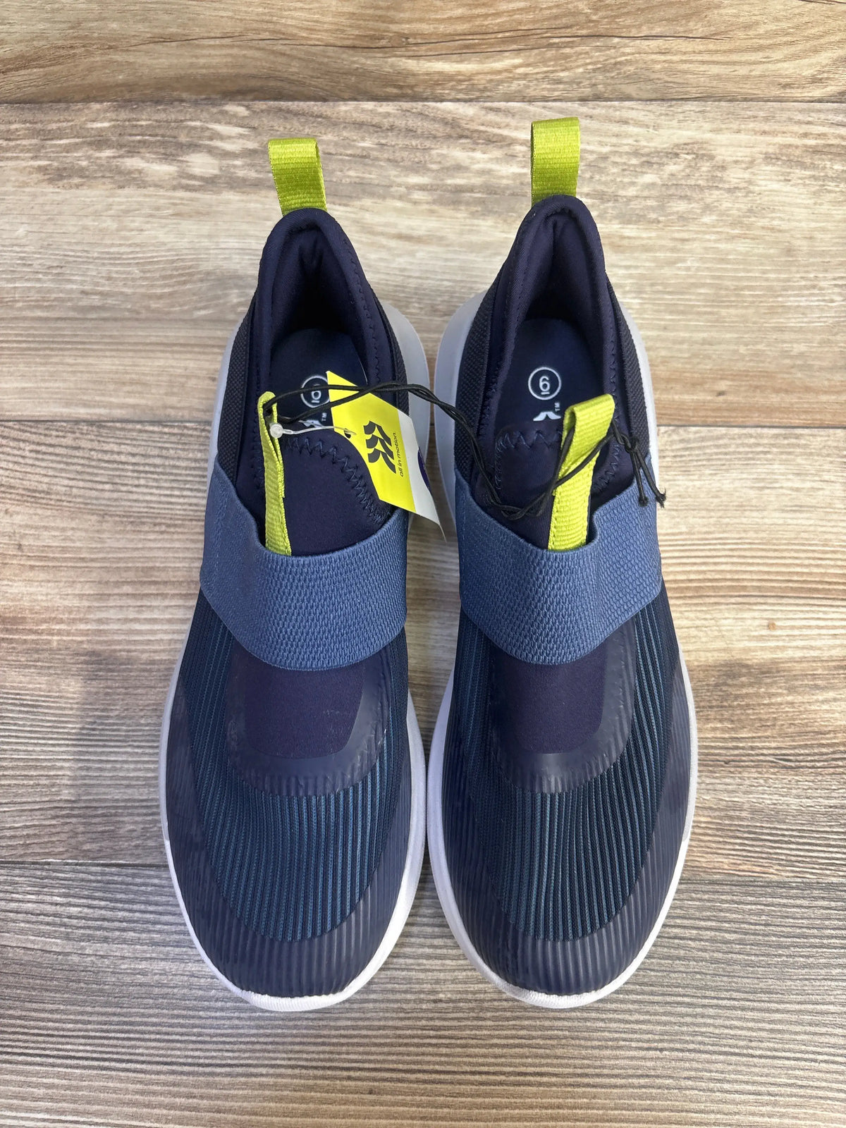 Top view of All In Motion navy slip-on sneakers with elastic strap and lime green heel tabs, size 6Y on wood floor