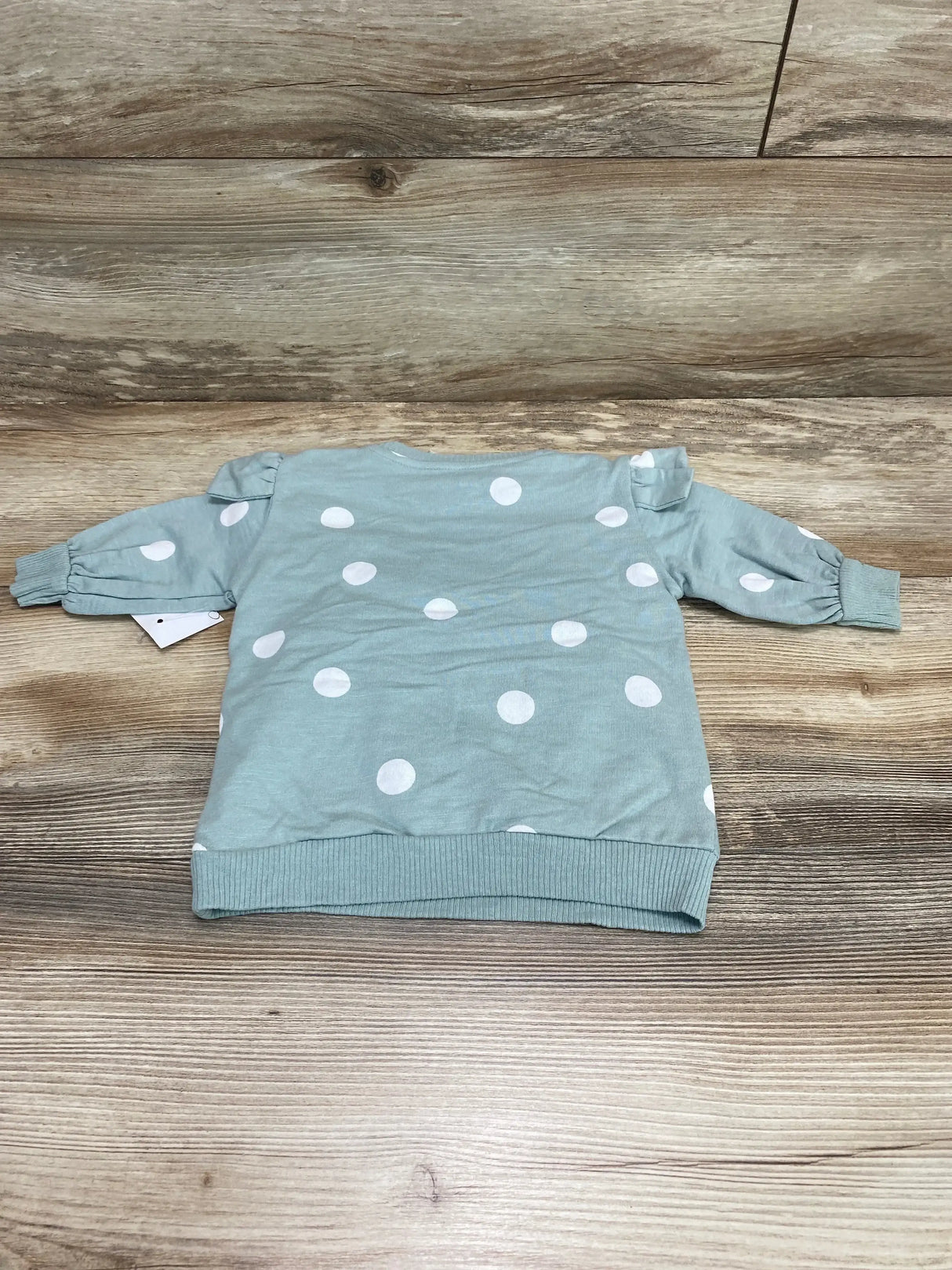 Back view of mint green polka dot baby sweatshirt dress showing puffed shoulders, ribbed cuffs and hem on wood background