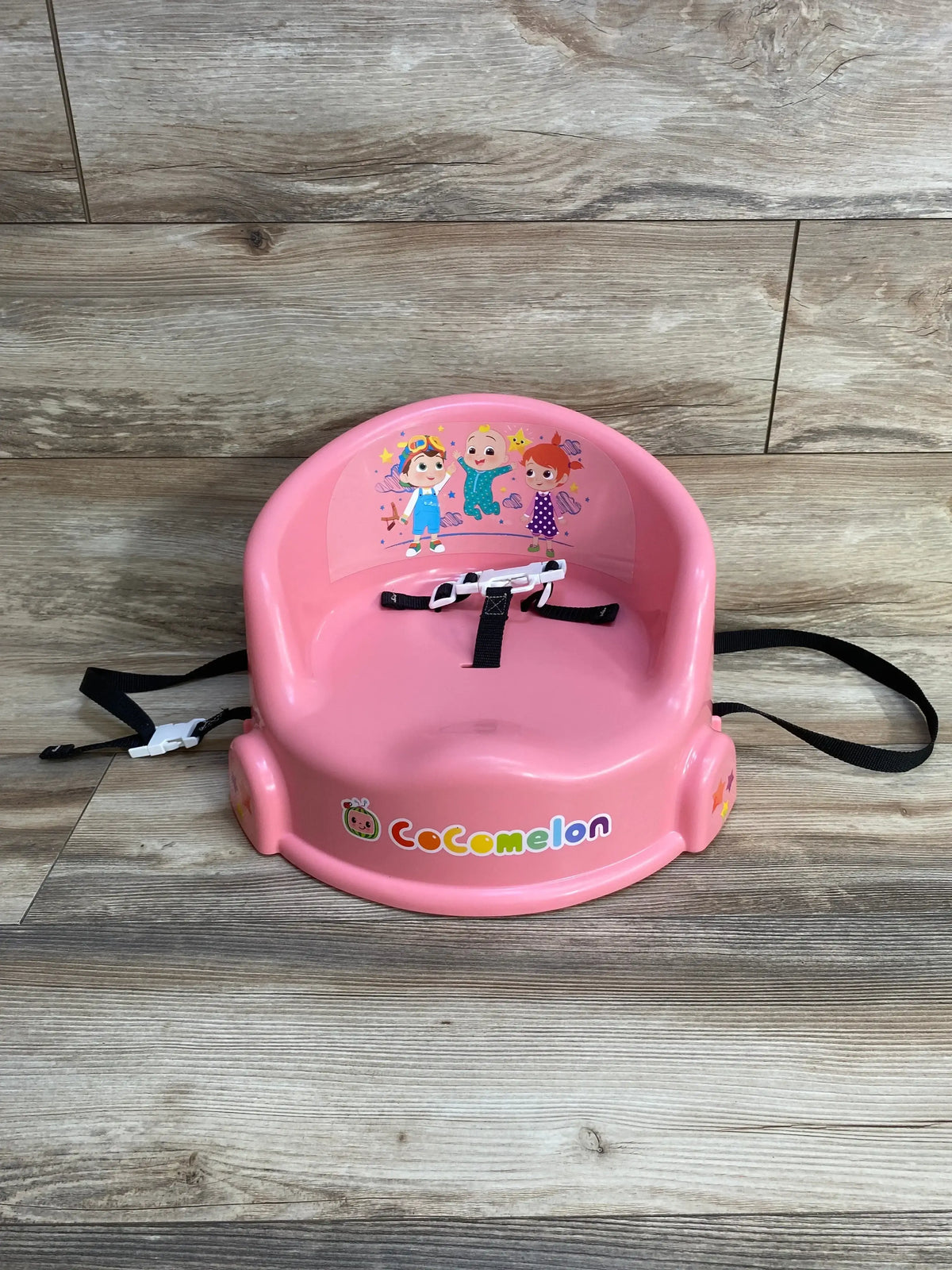 Front view of Cocomelon toddler seat showcasing molded back, safety harness straps and character decals on wood background