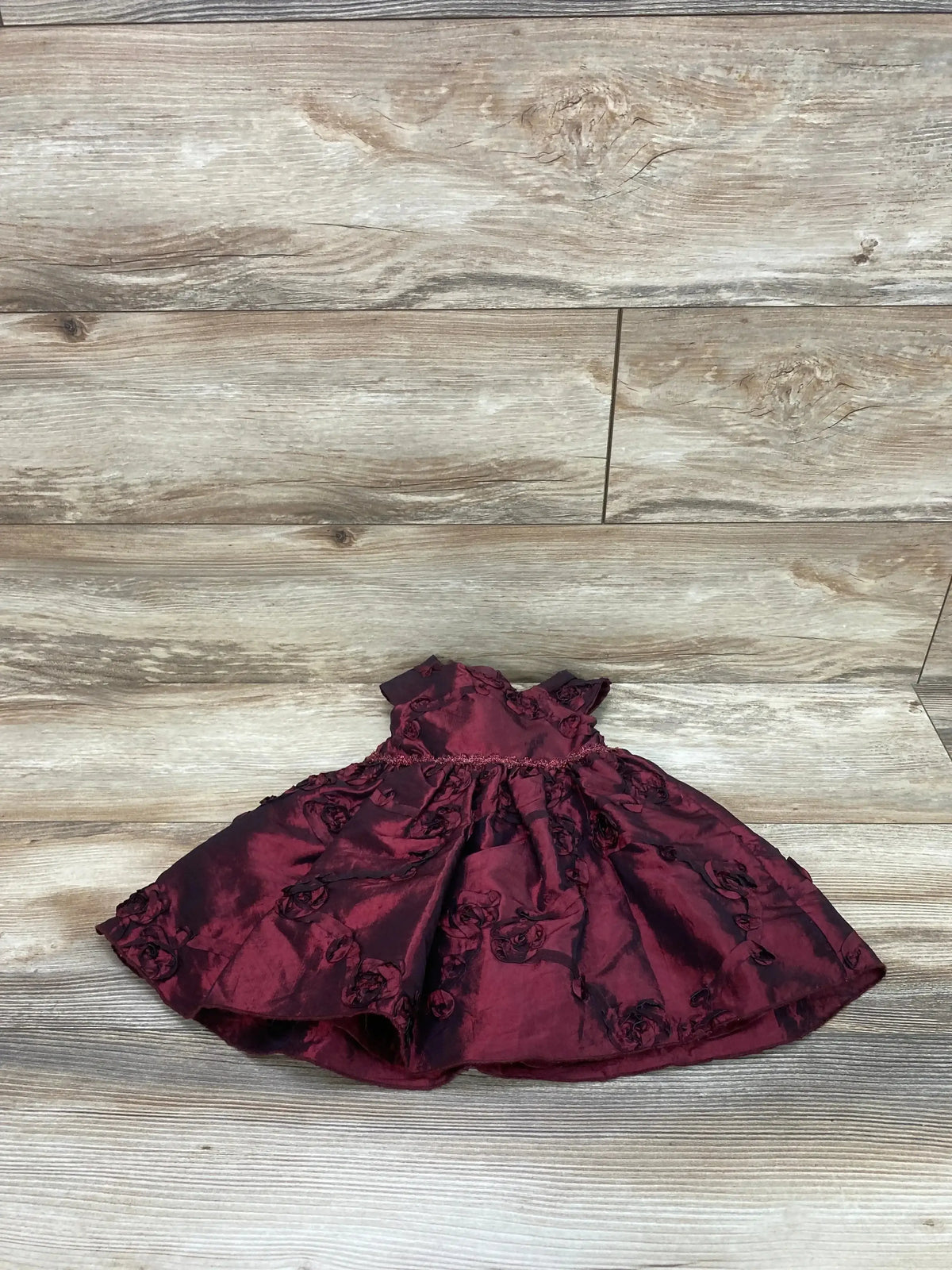 Front view of red cap-sleeve baby dress and matching bloomers with gathered waist and rosette texture on wood background