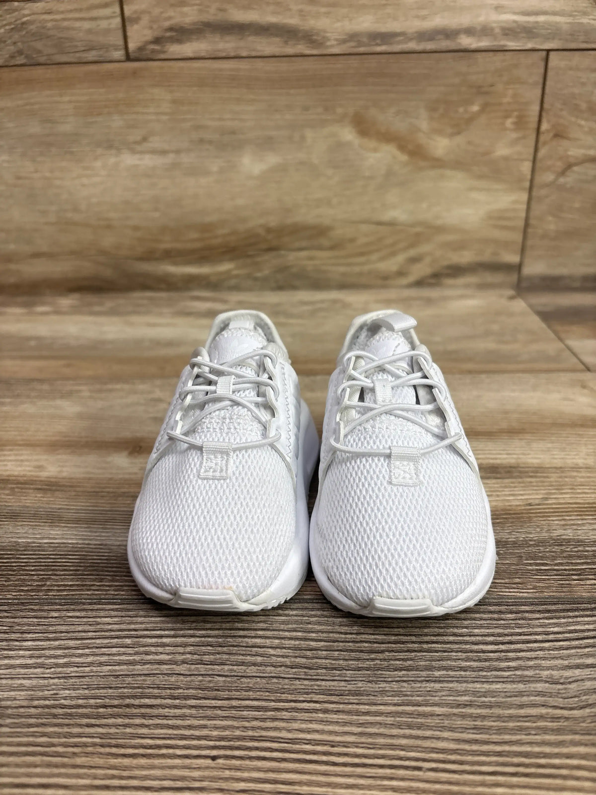 Front view of Adidas X_PLR sneakers showcasing white mesh uppers and laces on a wood floor