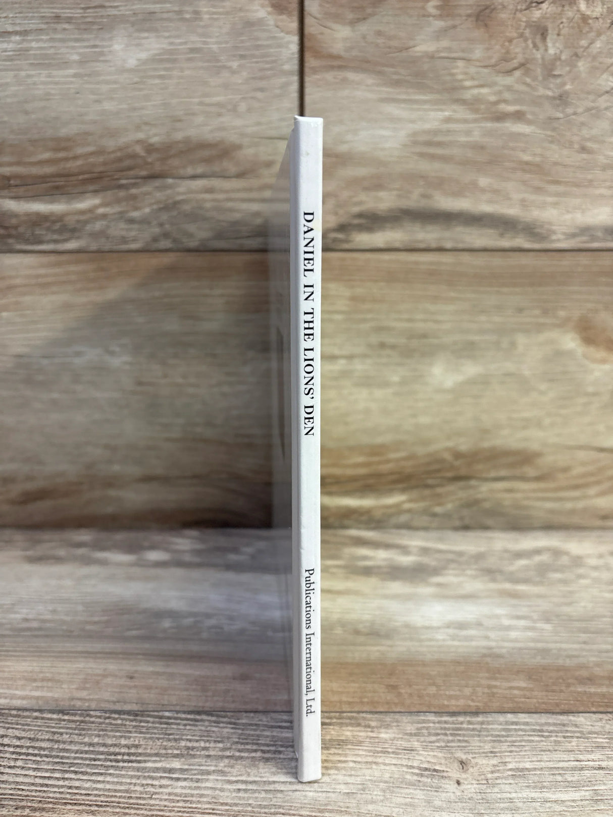Spine view of Daniel in the Lions' Den hardcover children's book showing white spine with title and publisher on wood background