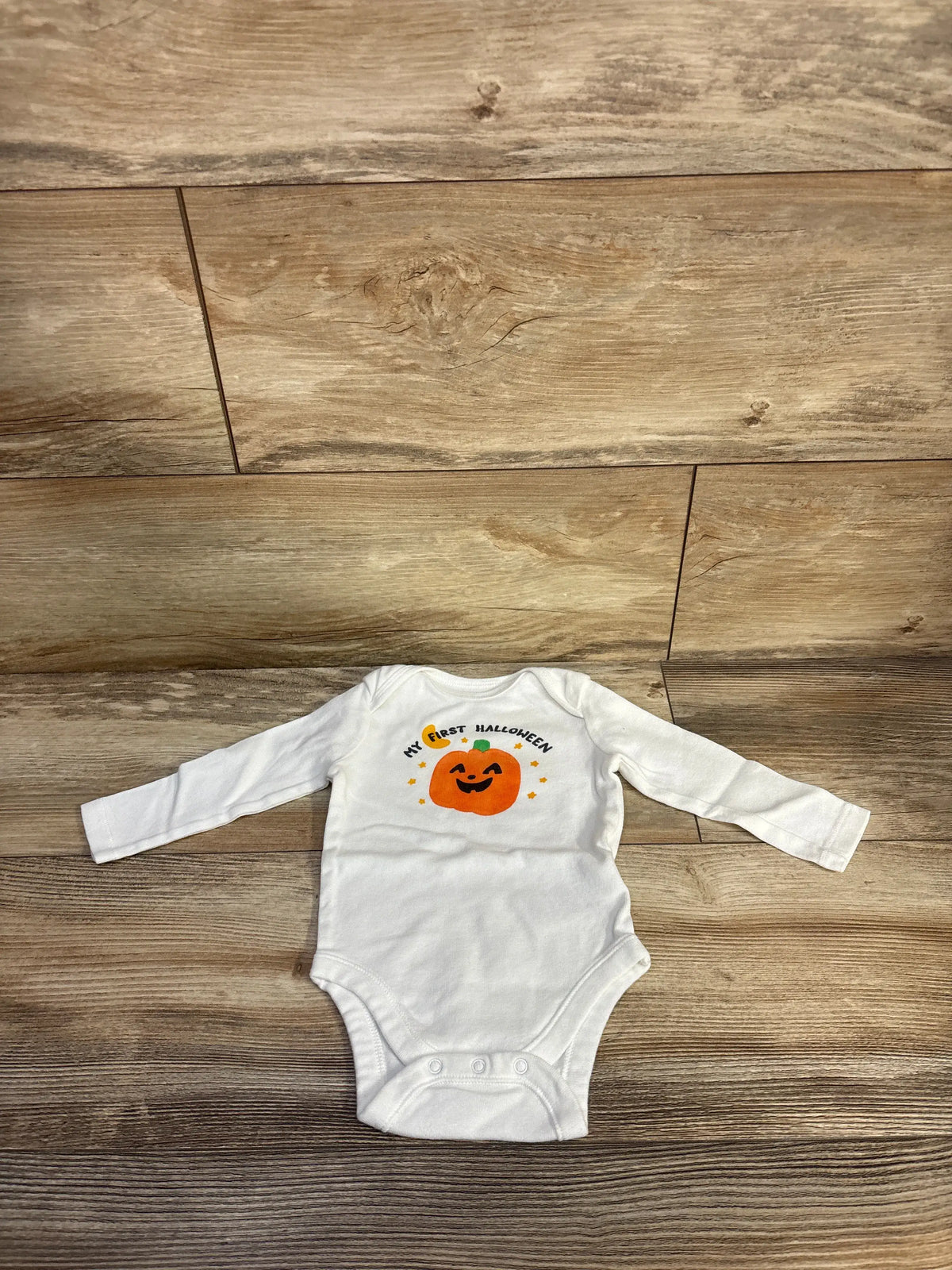 Front view of white Old Navy My First Halloween bodysuit showcasing a pumpkin and My First Halloween graphic with a wood floor background