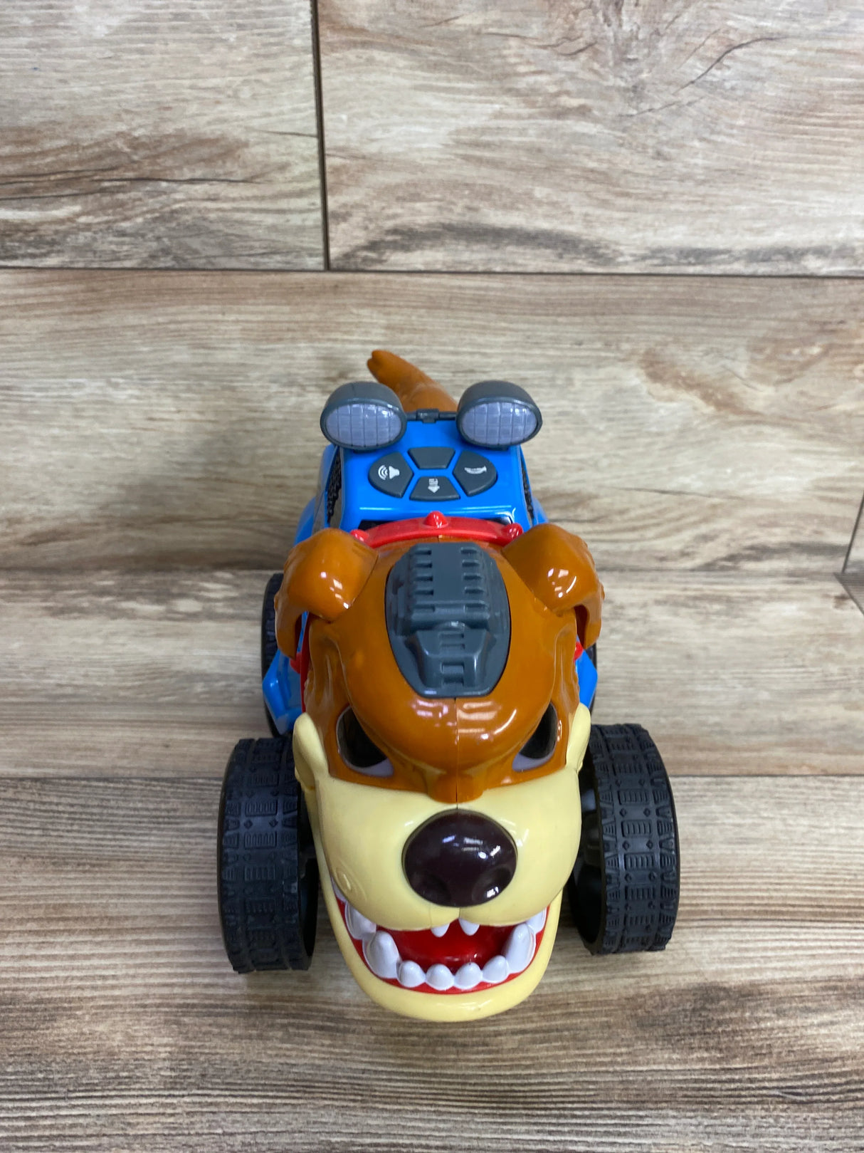 Front view of a blue and brown dog-themed children's toy car with black wheels on wooden floor