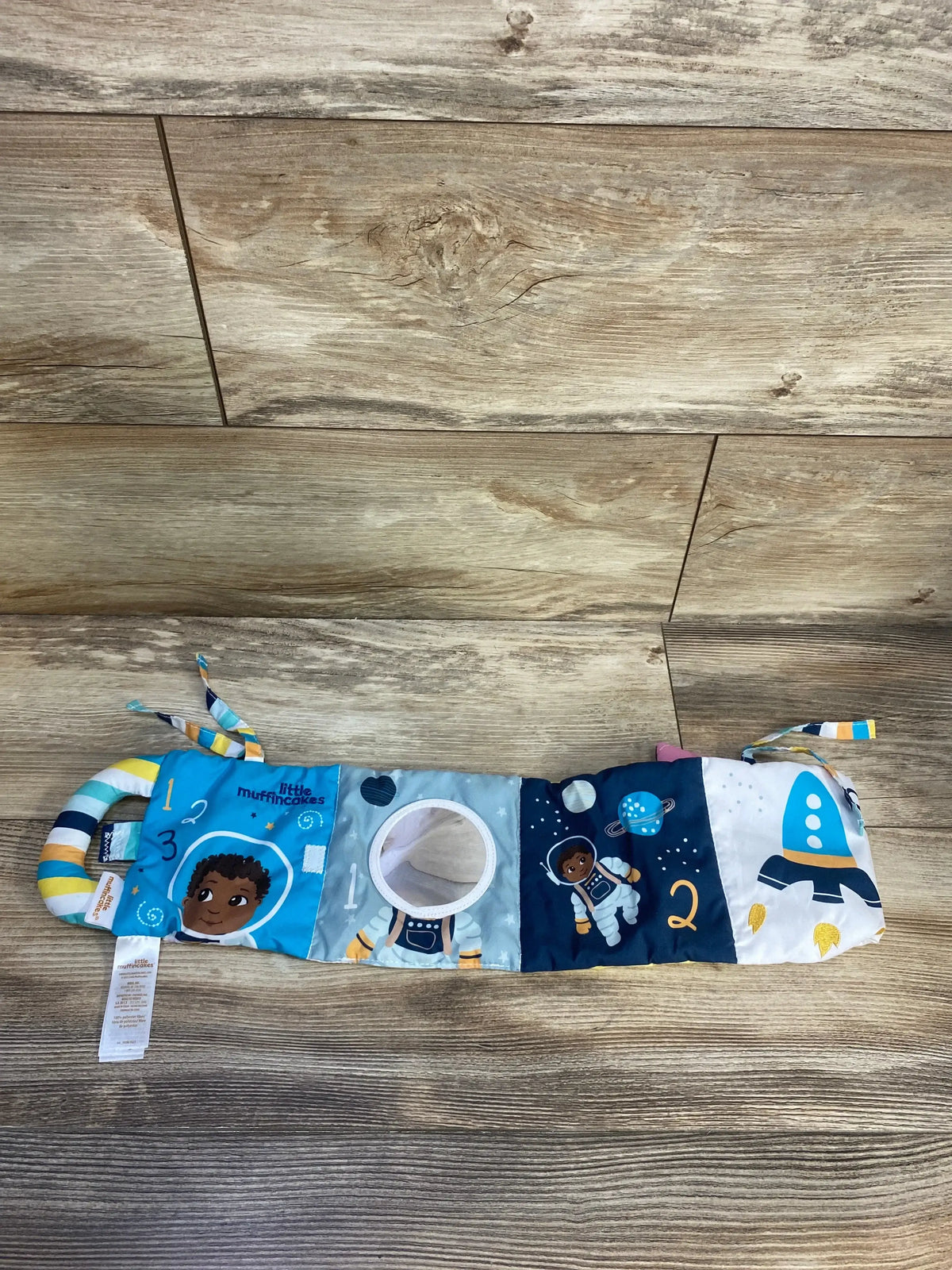 Top-down view of Ashton Blue soft book showing mirror, numbered astronaut panels, rocket print, and striped handle on wood