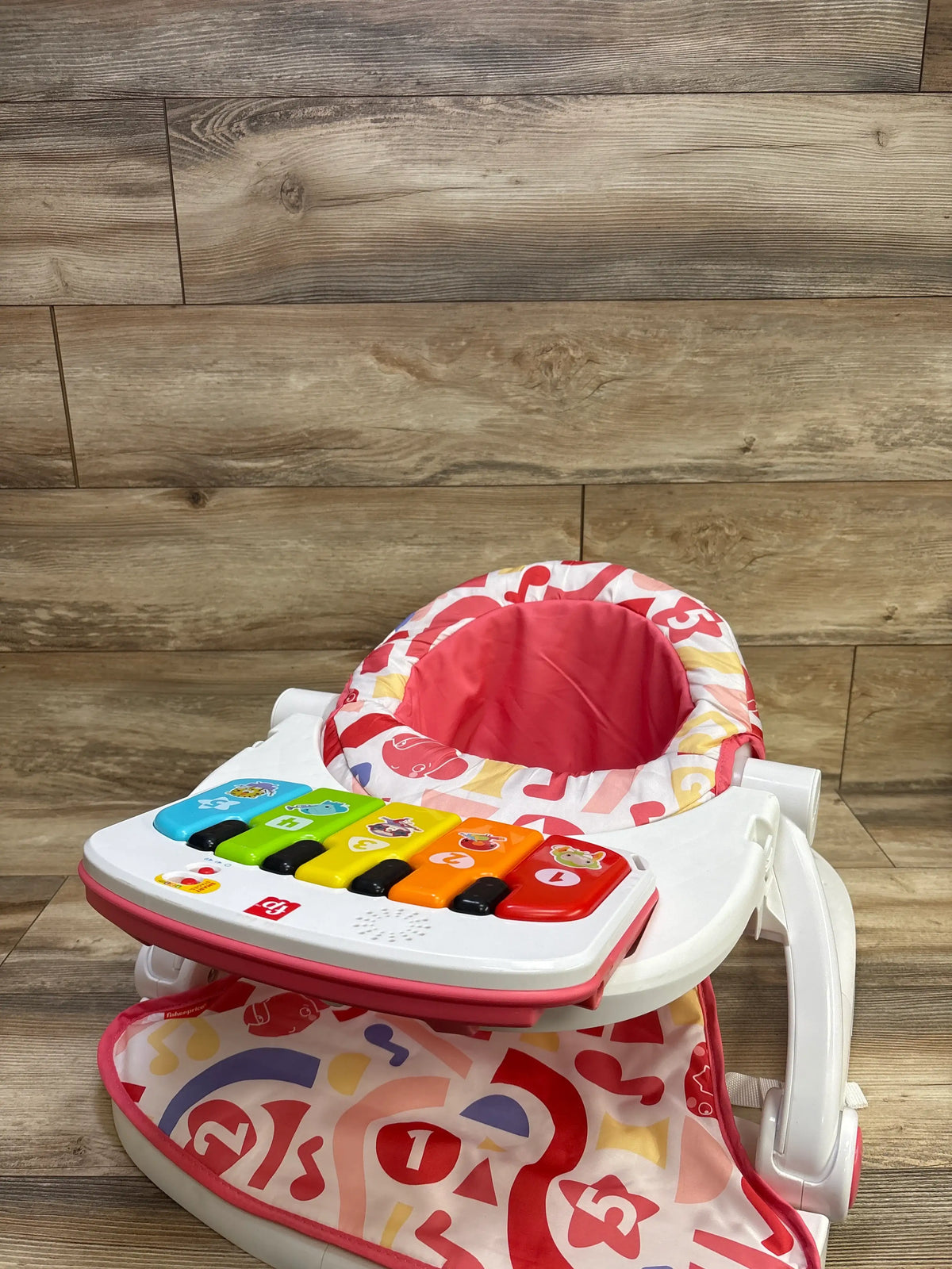 Front view of Fisher-Price Deluxe Kick & Play Sit-Me-Up Floor Seat showcasing colorful musical keyboard with wood plank background