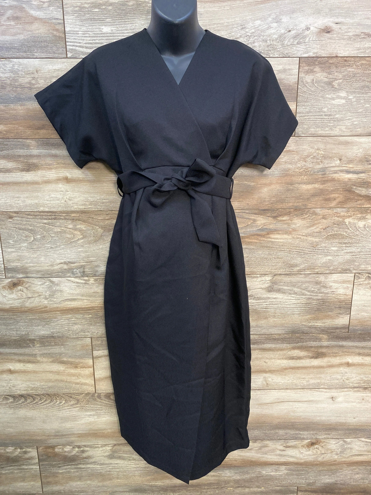 Black kimono wrap dress with short sleeves and waist tie on mannequin, wooden background