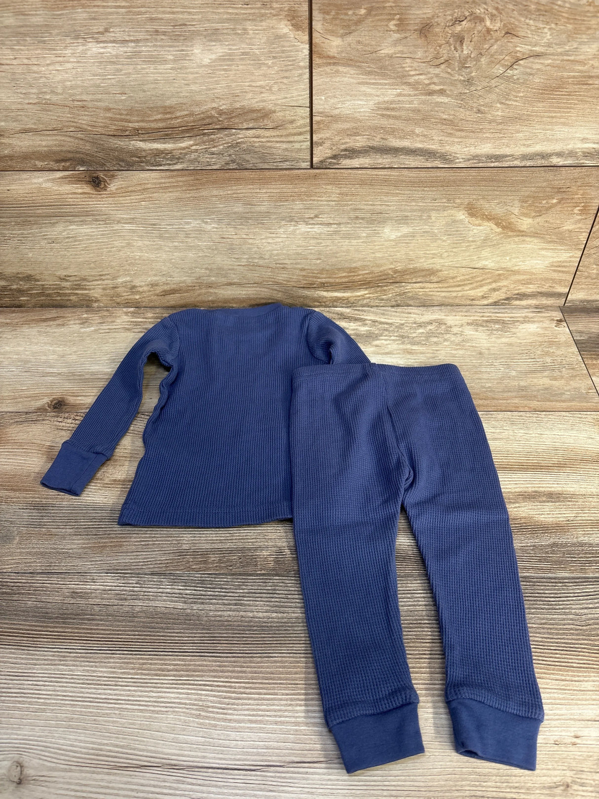 Flat lay of blue waffle-knit 2-piece baby pajama set, long-sleeve top and cuffed pants on wood background