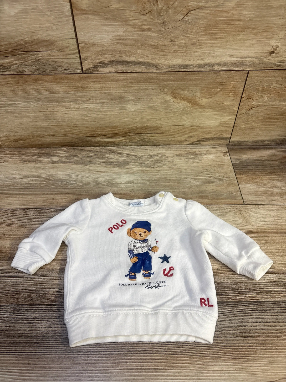 Front view of white Ralph Lauren Polo Bear pullover sweatshirt showcasing a Polo Bear graphic on a wood floor