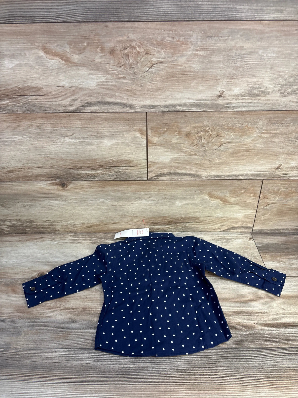 Front view of Cat & Jack navy polka dot button-up shirt with long sleeves and button cuffs on wood-look background