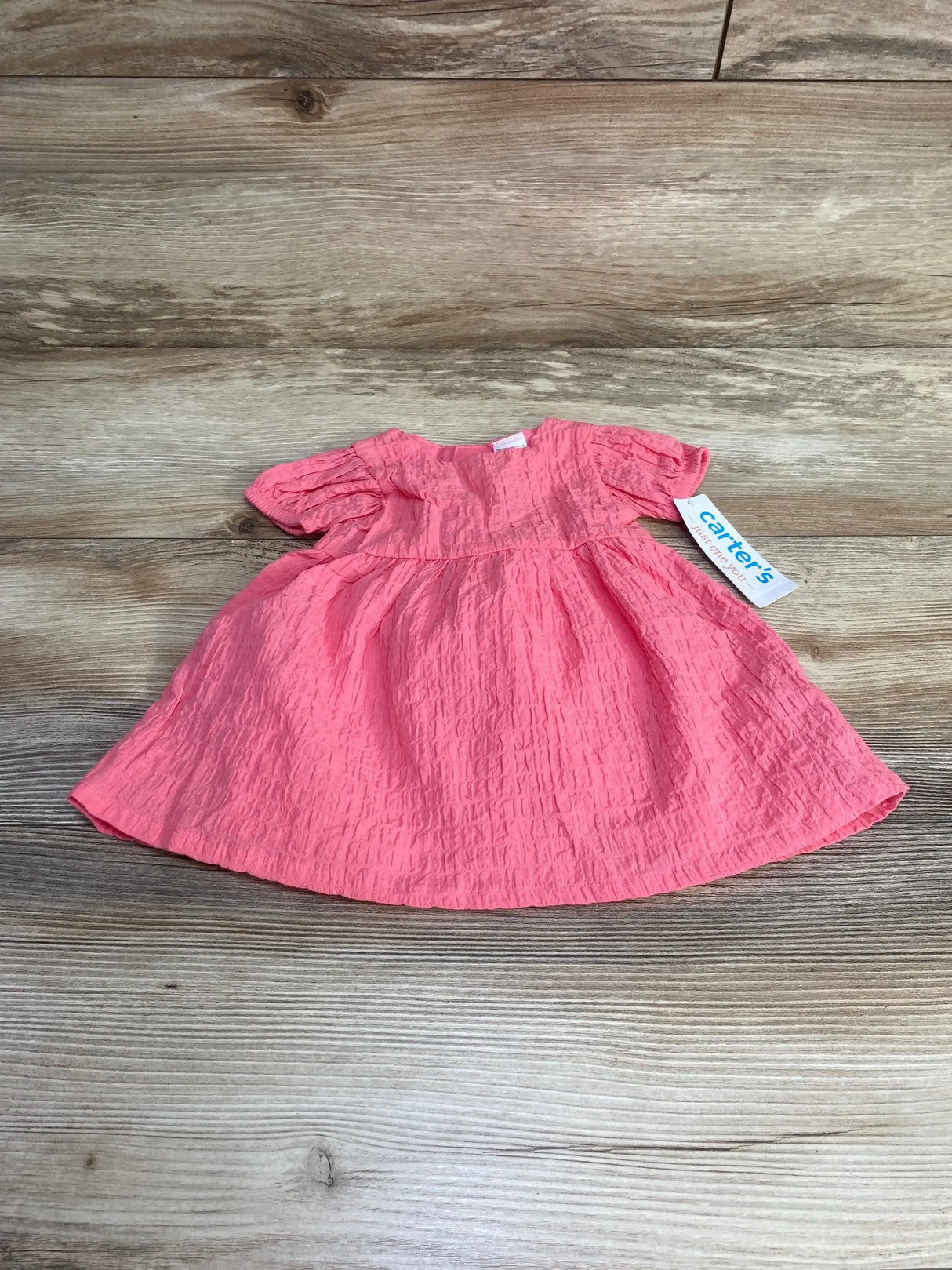 Top down view of newborn pink baby dress showing crinkled texture, puff sleeves and gathered empire waist on wood background