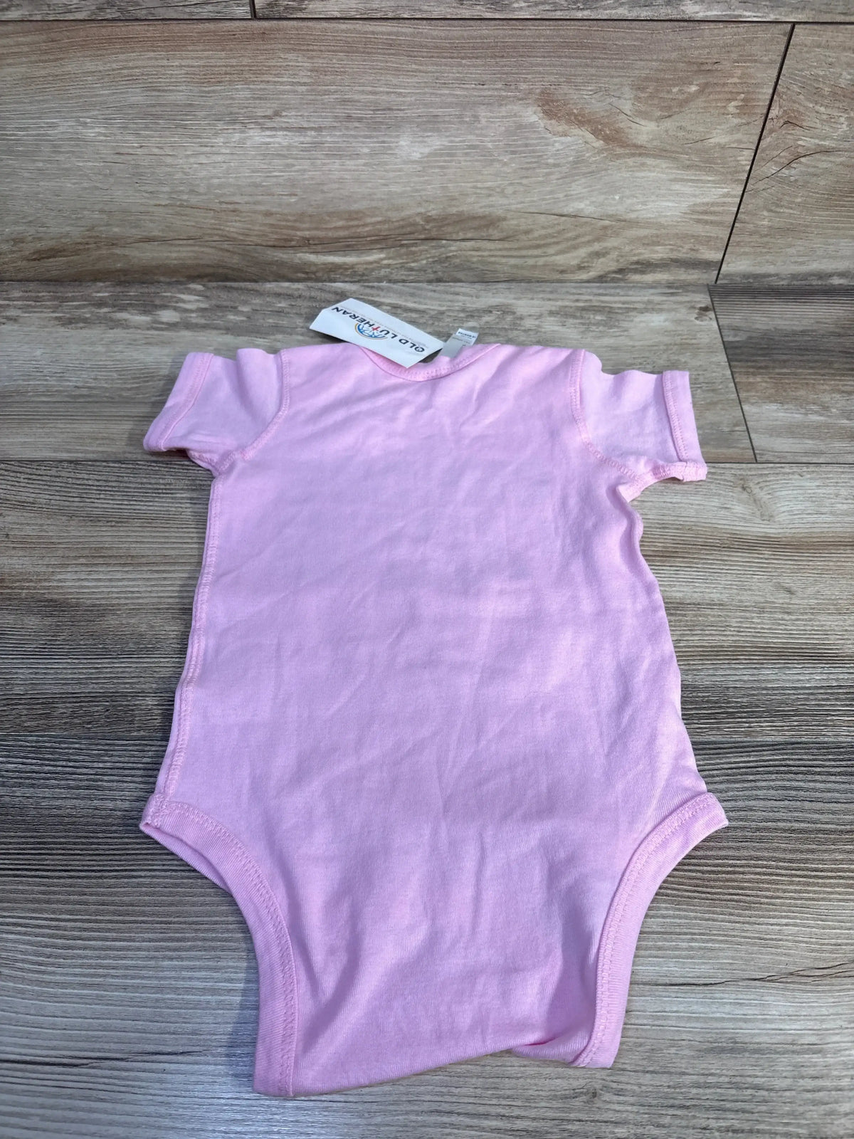 Flat lay of Rabbit Skins pink 18-month bodysuit showing the back and short sleeves on light wood background