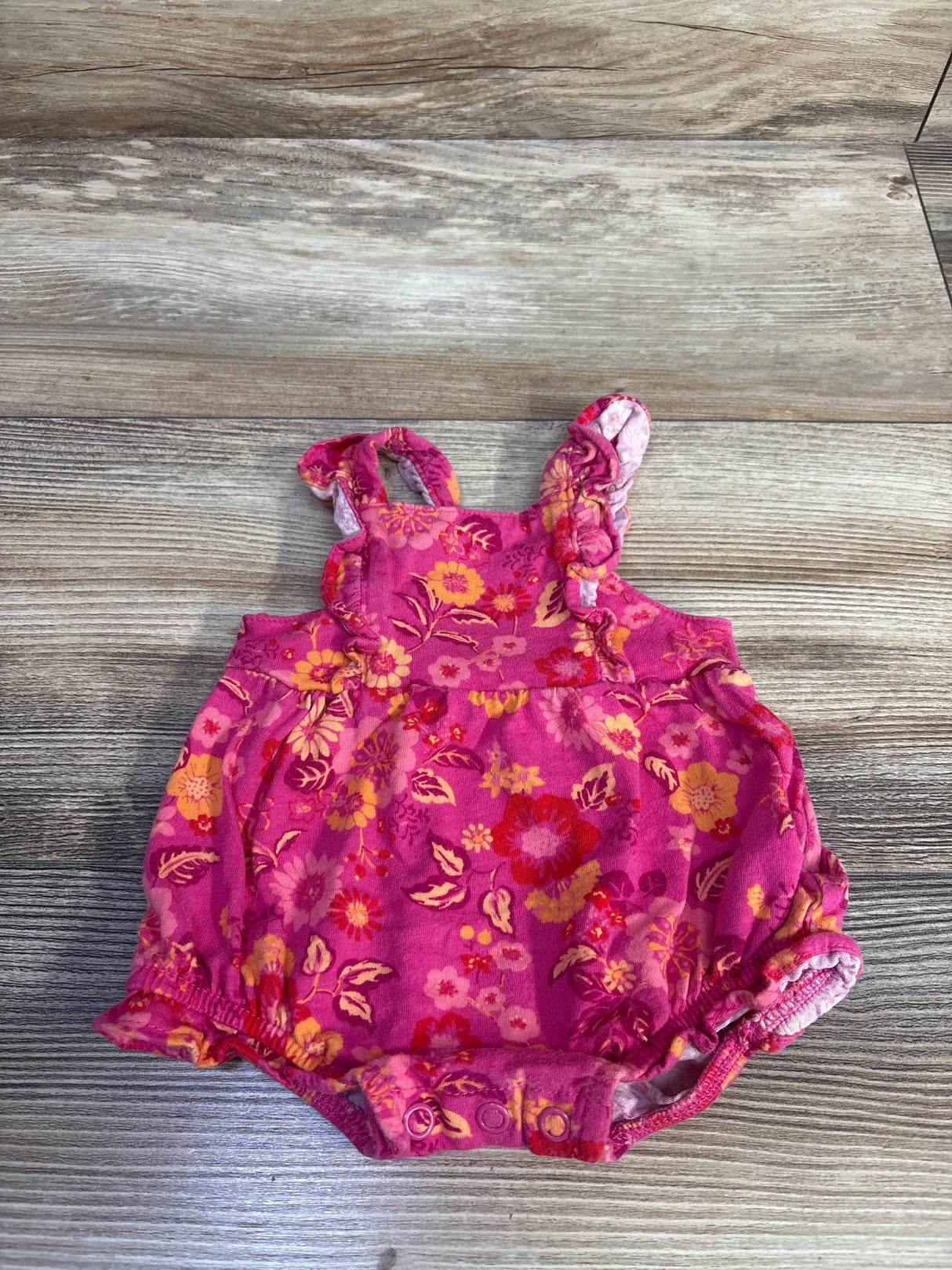 Top-down view of pink floral Carter's bubble romper showing ruffled shoulder straps and snap crotch on wood background