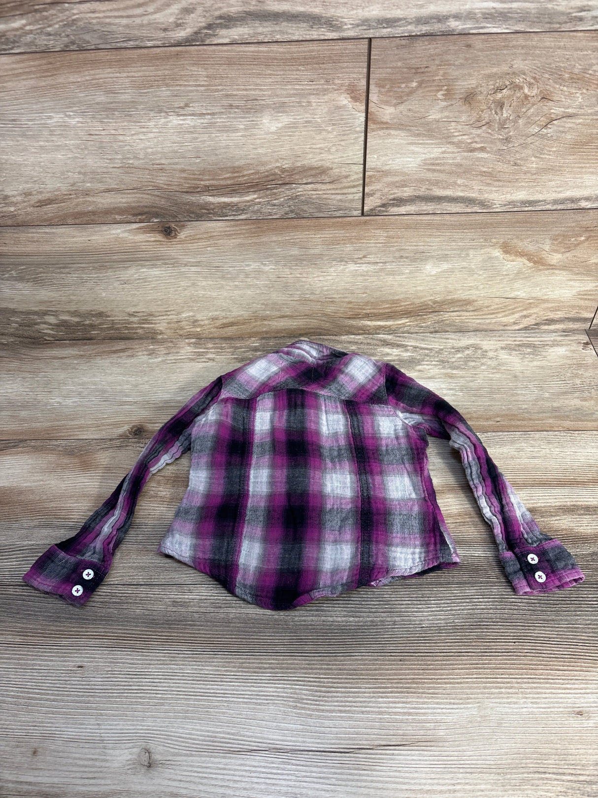 Purple, black, and white plaid long sleeve shirt laid flat on wooden floor
