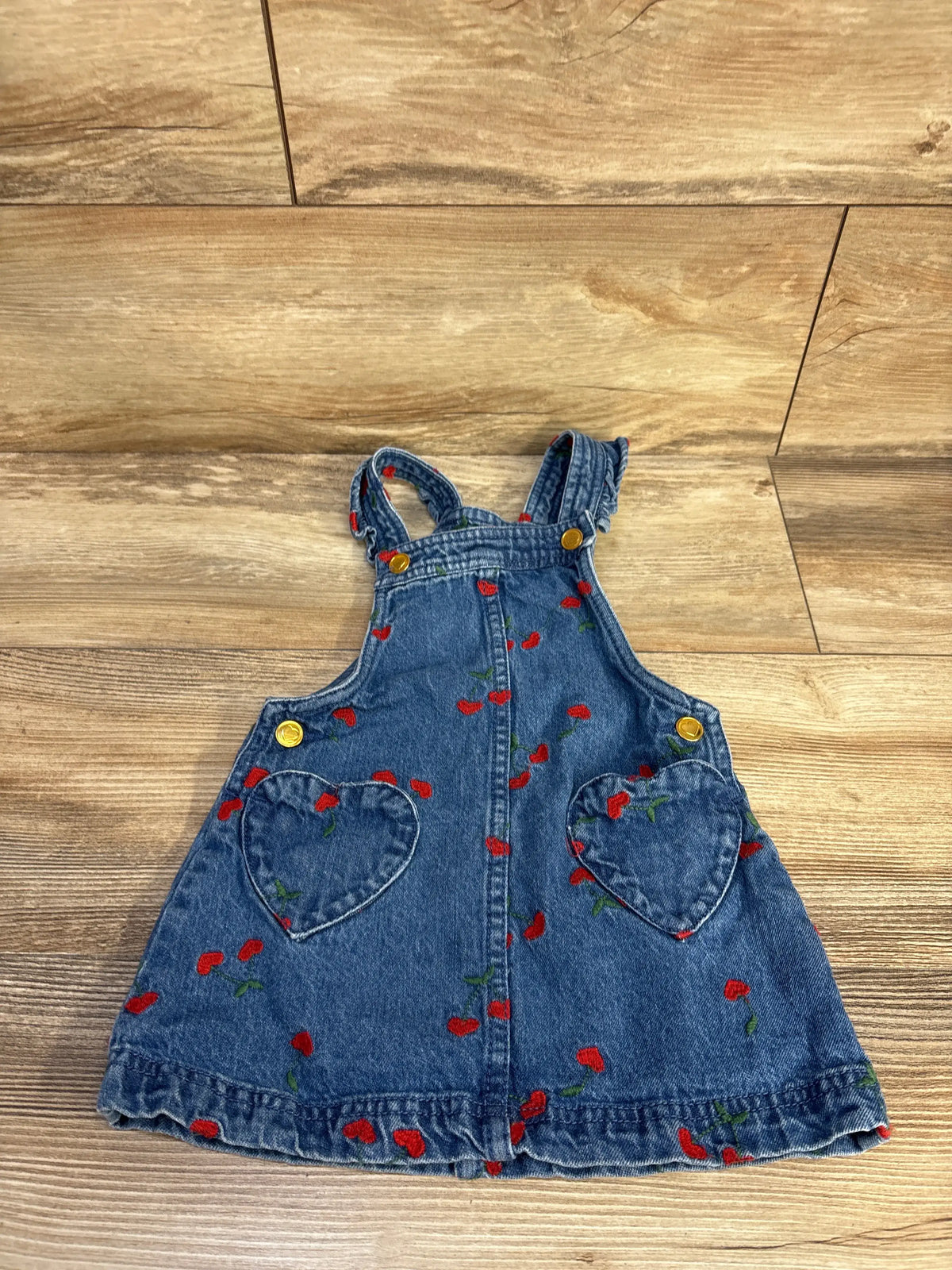 Front view of Isaac Mizrahi embroidered denim skirtall showcasing cherry embroidery, heart pockets, and ruffled hem on a wood-look floor