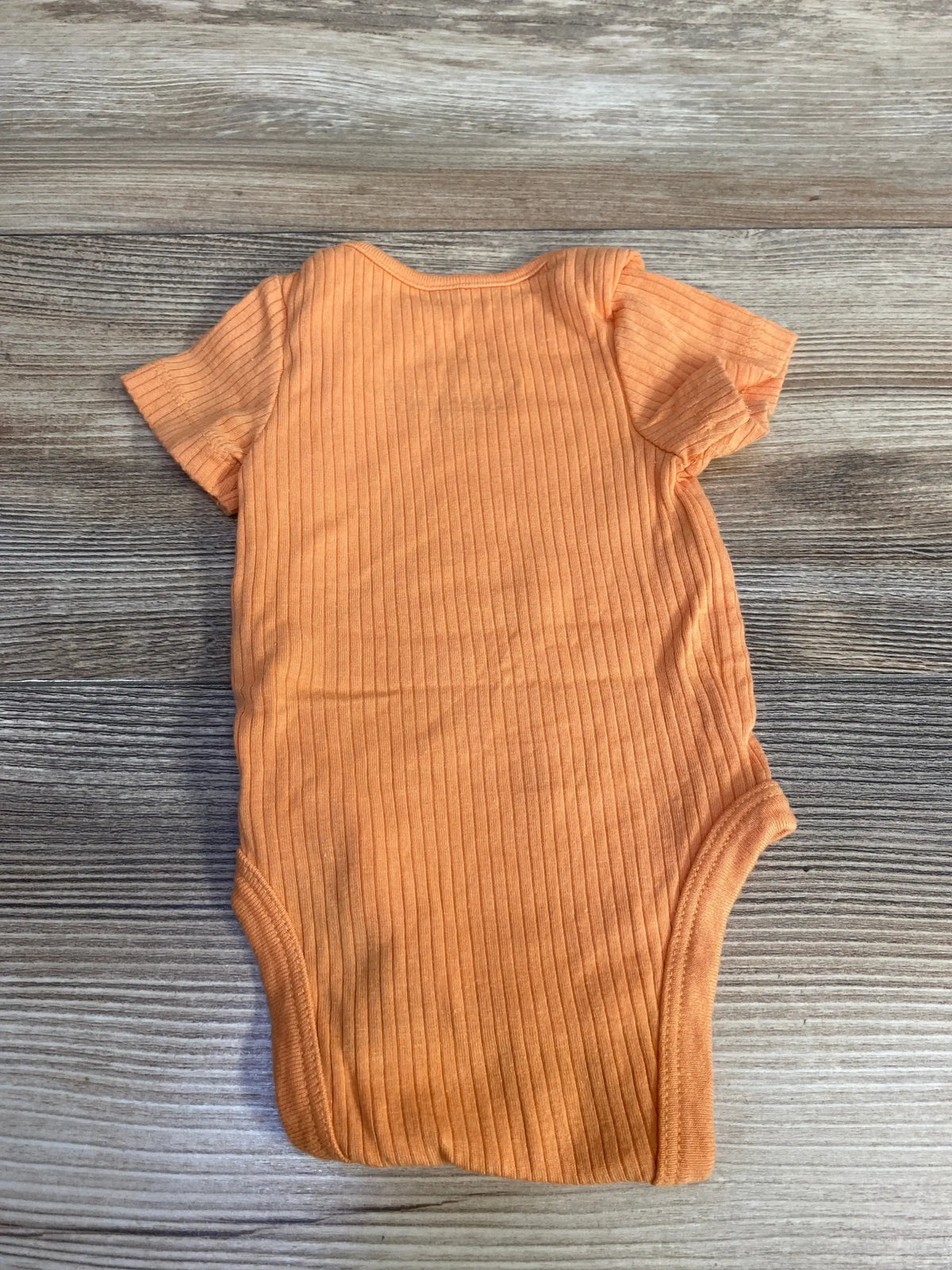 Back view of newborn orange ribbed bodysuit showing short sleeves and vertical ribbing on wood surface