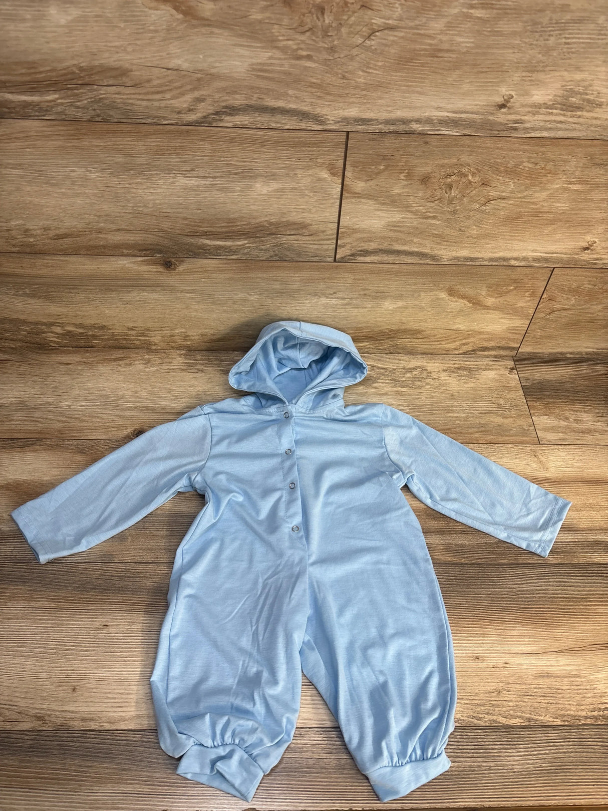 Light blue hooded baby romper with buttons, long sleeves, and cuffs on wood background