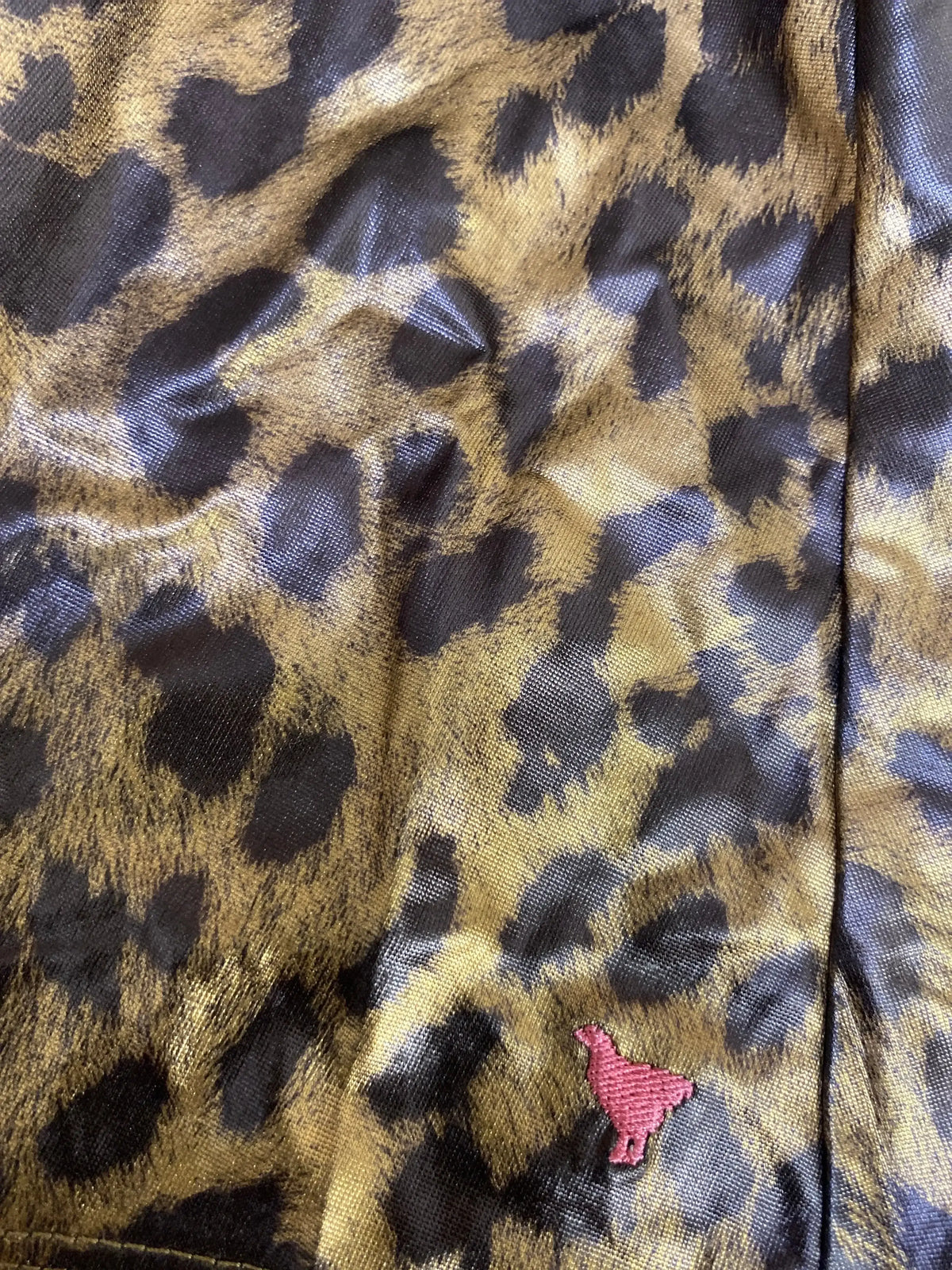 Close-up of shiny leopard print fabric with a small pink embroidered bird detail