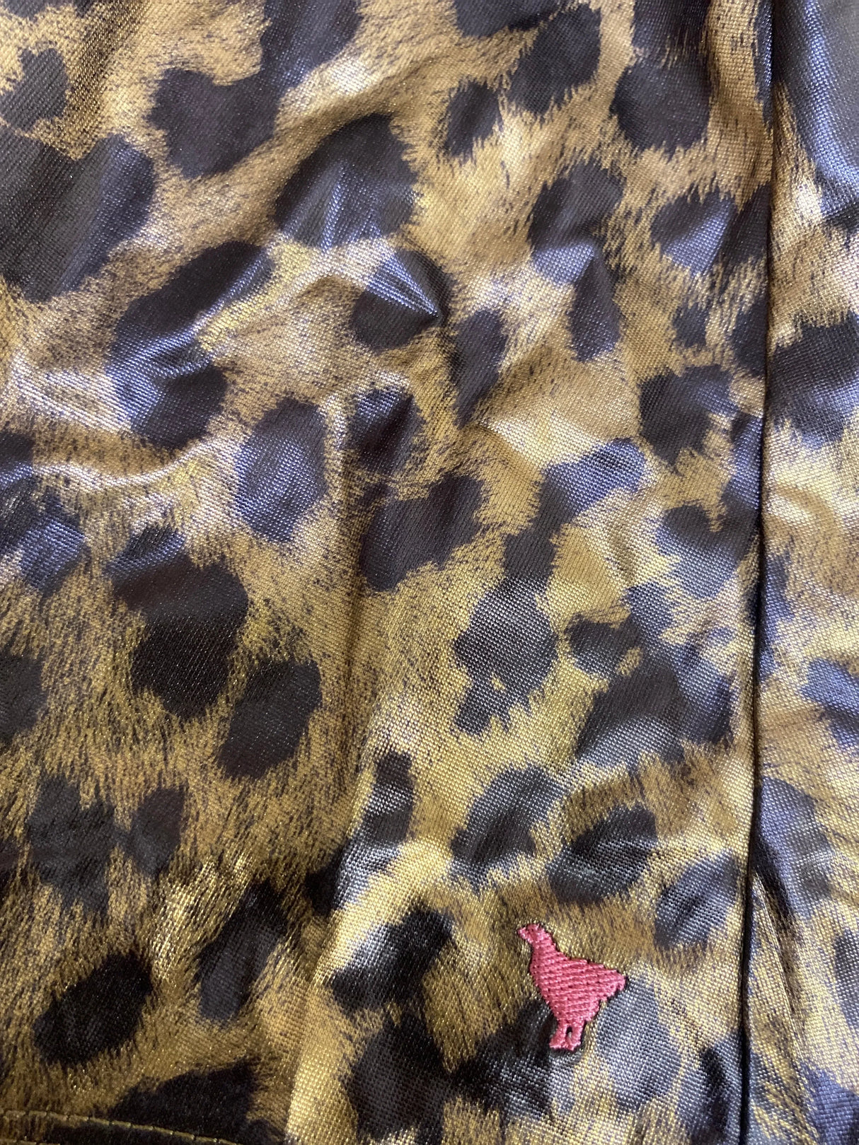 Close-up of shiny leopard print fabric with a small pink embroidered bird detail