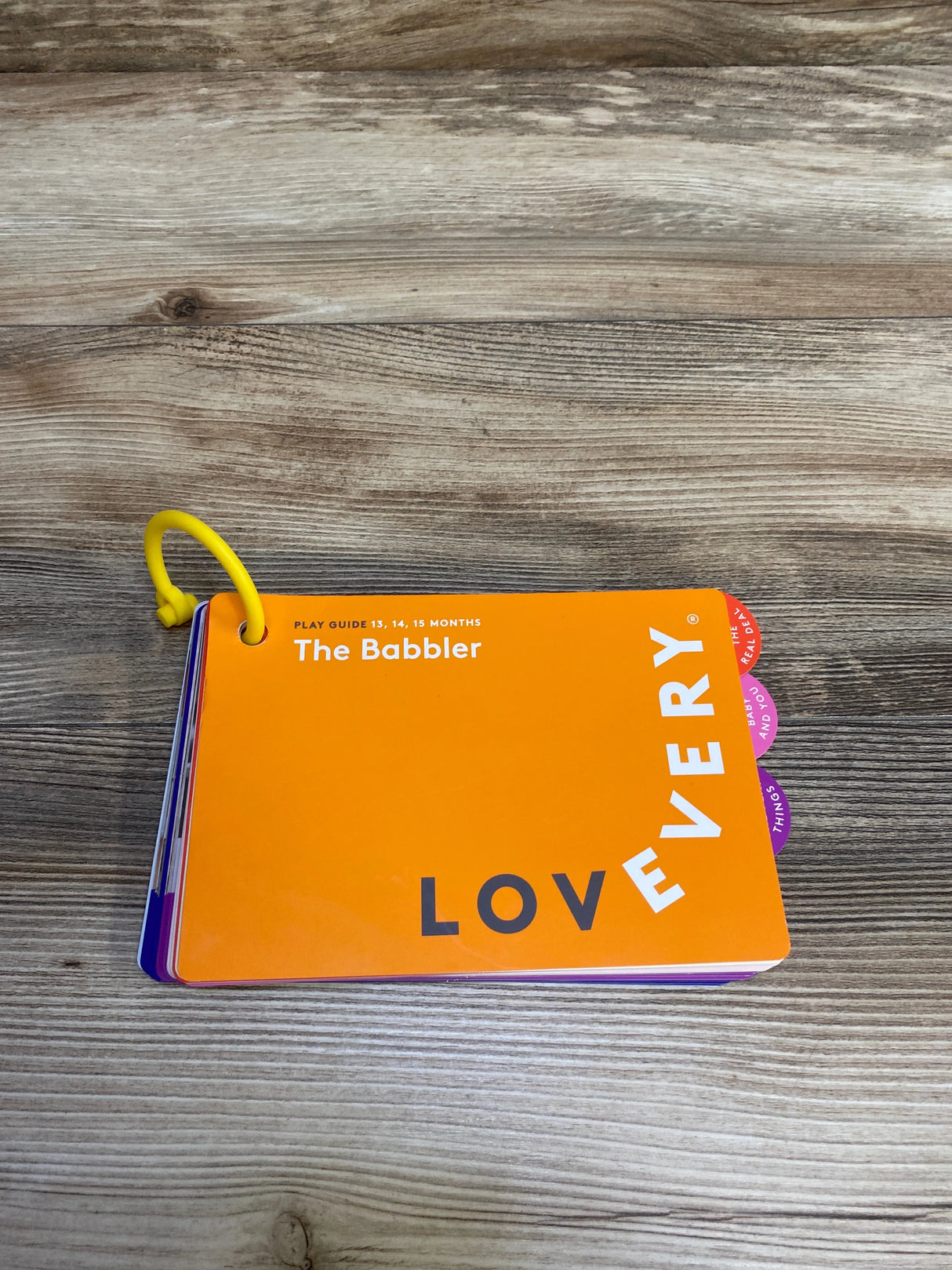 orange baby board book titled The Babbler for 13-15 months by Lovevery on wood surface