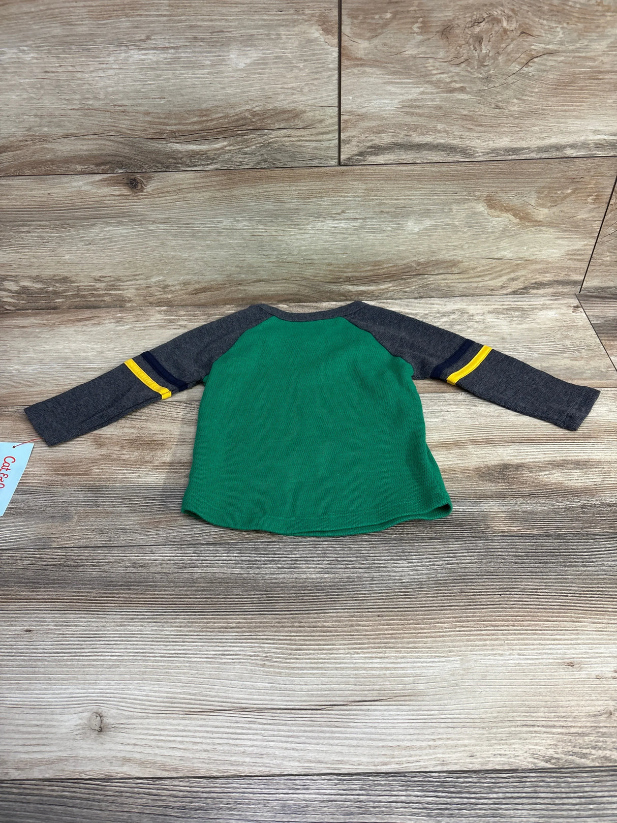 Green and gray long sleeve toddler shirt with yellow stripes on sleeves on wooden floor