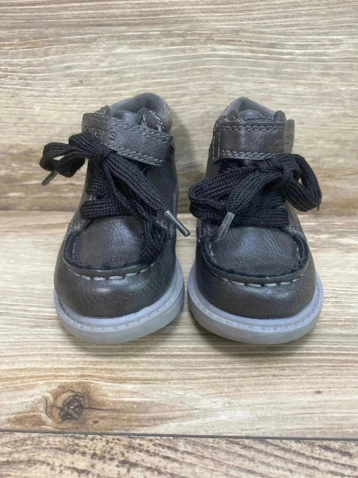 Front view of Carter’s Norman boys’ grey ankle boots with Velcro strap, black laces and translucent sole on wood background