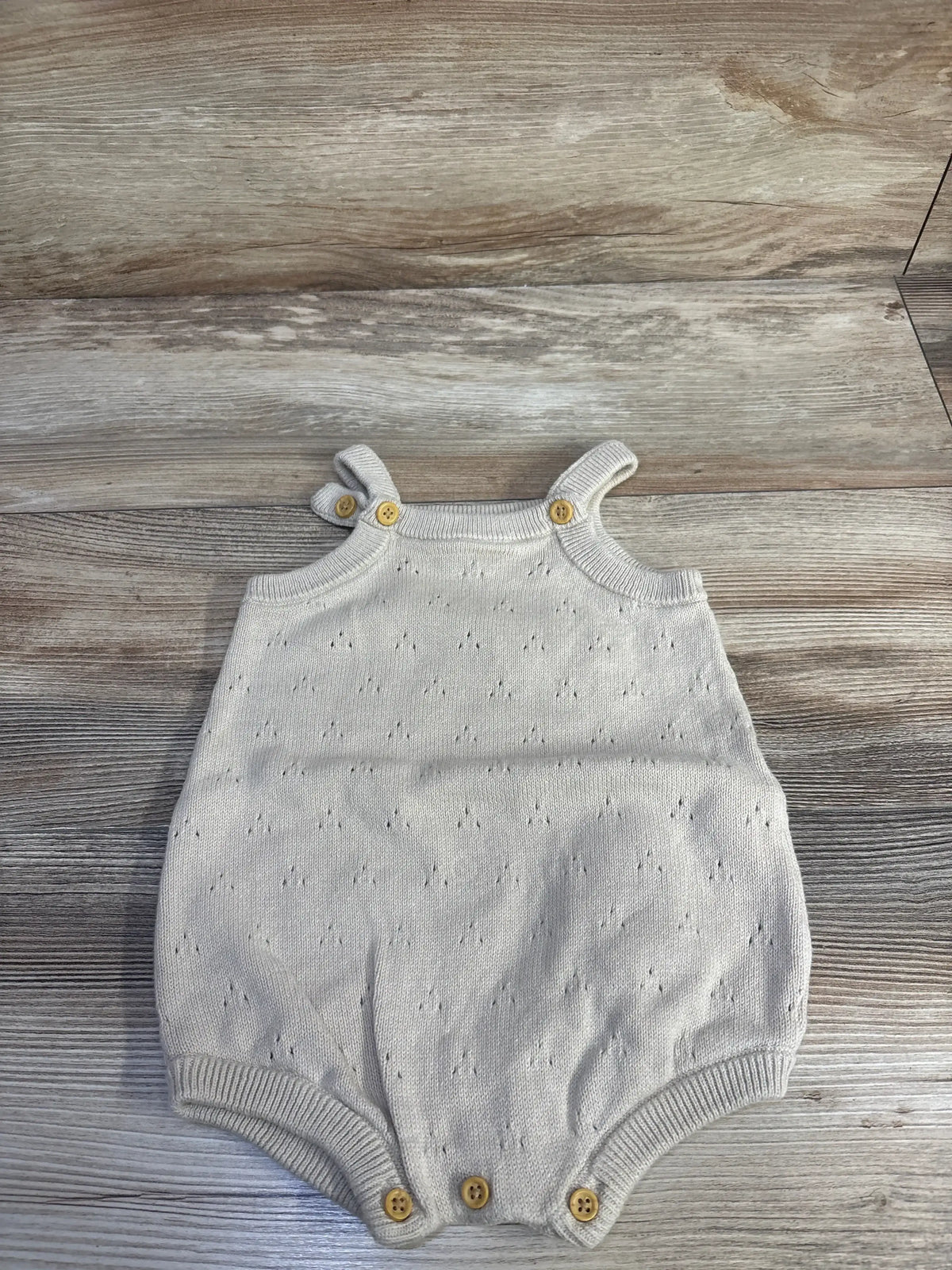 Top view of Little Planet tan eyelet bubble romper (12m) showing wooden button straps and ribbed trim on wood background