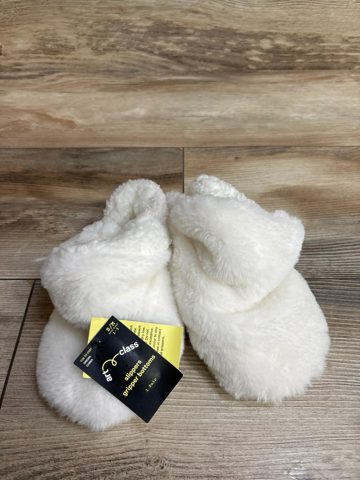 soft white fluffy baby slippers with gripper bottoms on wood floor