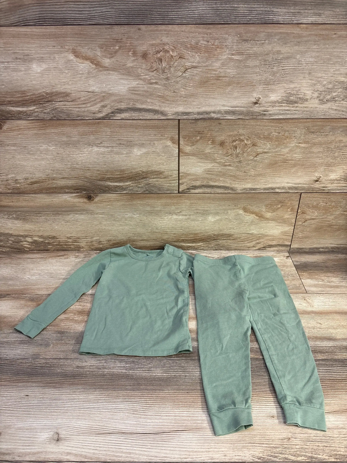 Flat lay of Magnetic Me green 2-piece toddler pajama set showing long-sleeve top with shoulder snap and cuffed pants on wood