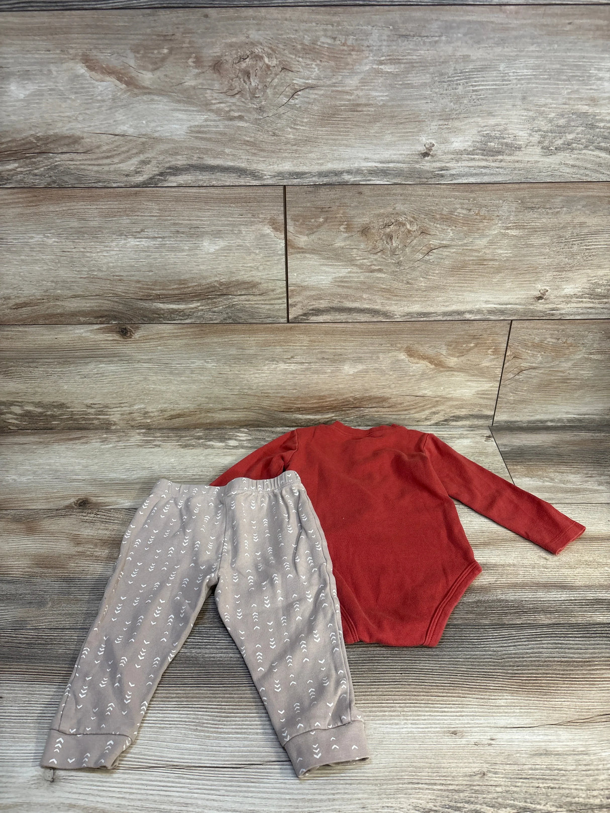 Red long sleeve baby bodysuit and gray patterned pants on wood background