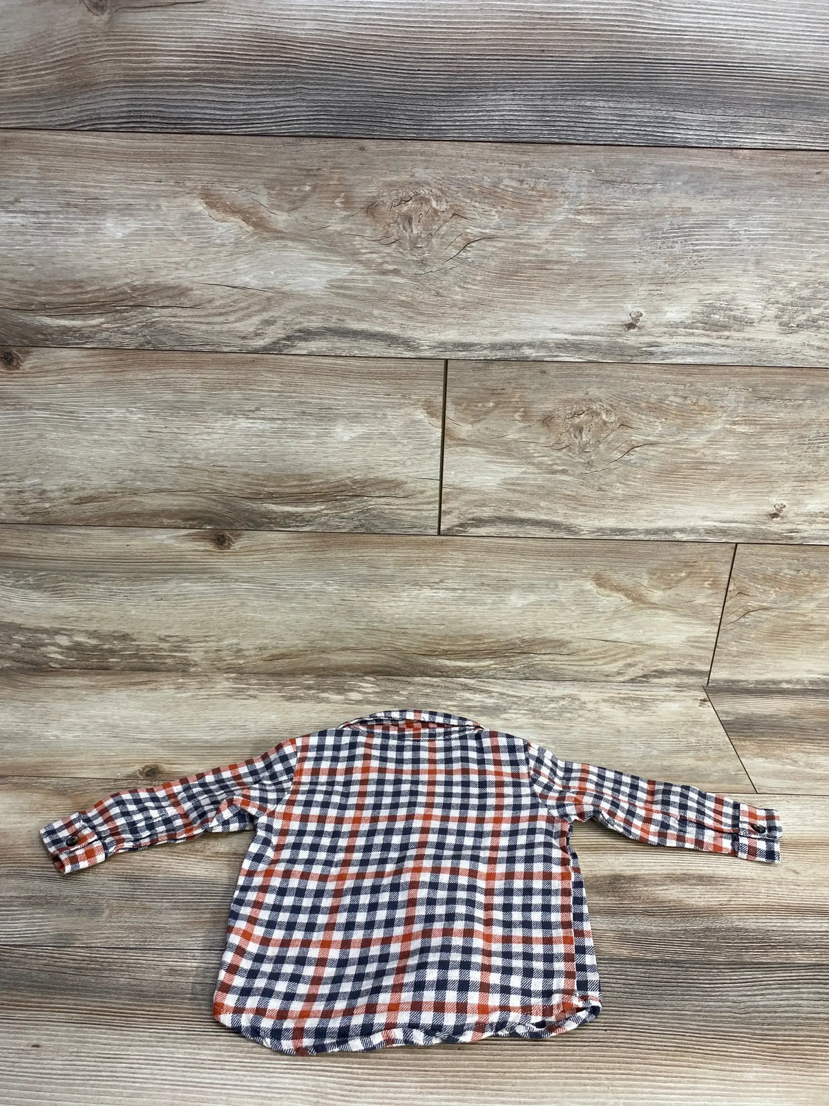 Long sleeve toddler plaid flannel shirt in red, white, and navy on wood background