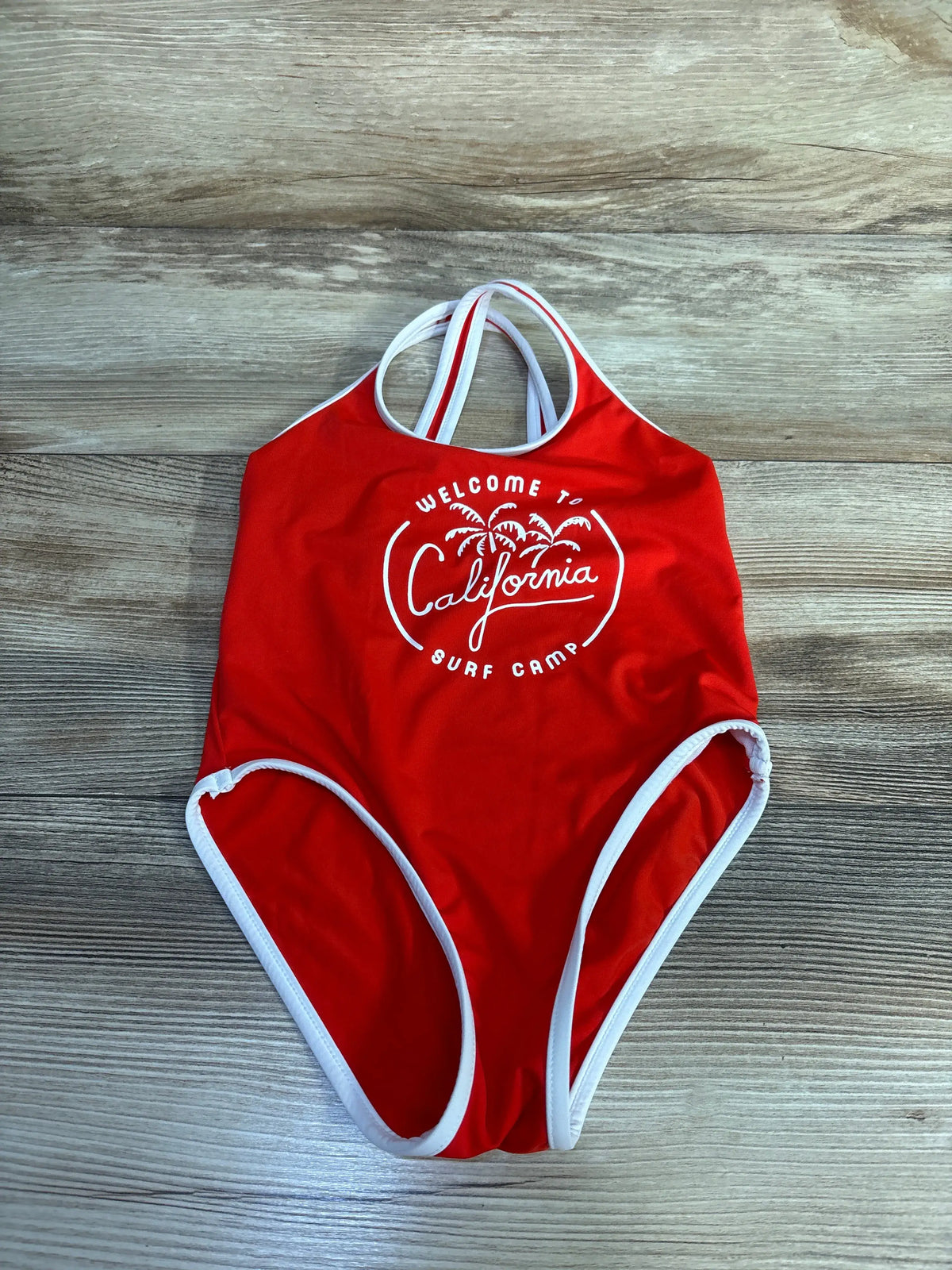Front view of Zara red one-piece swimsuit with white trim and Welcome to California Surf Camp graphic on wood background