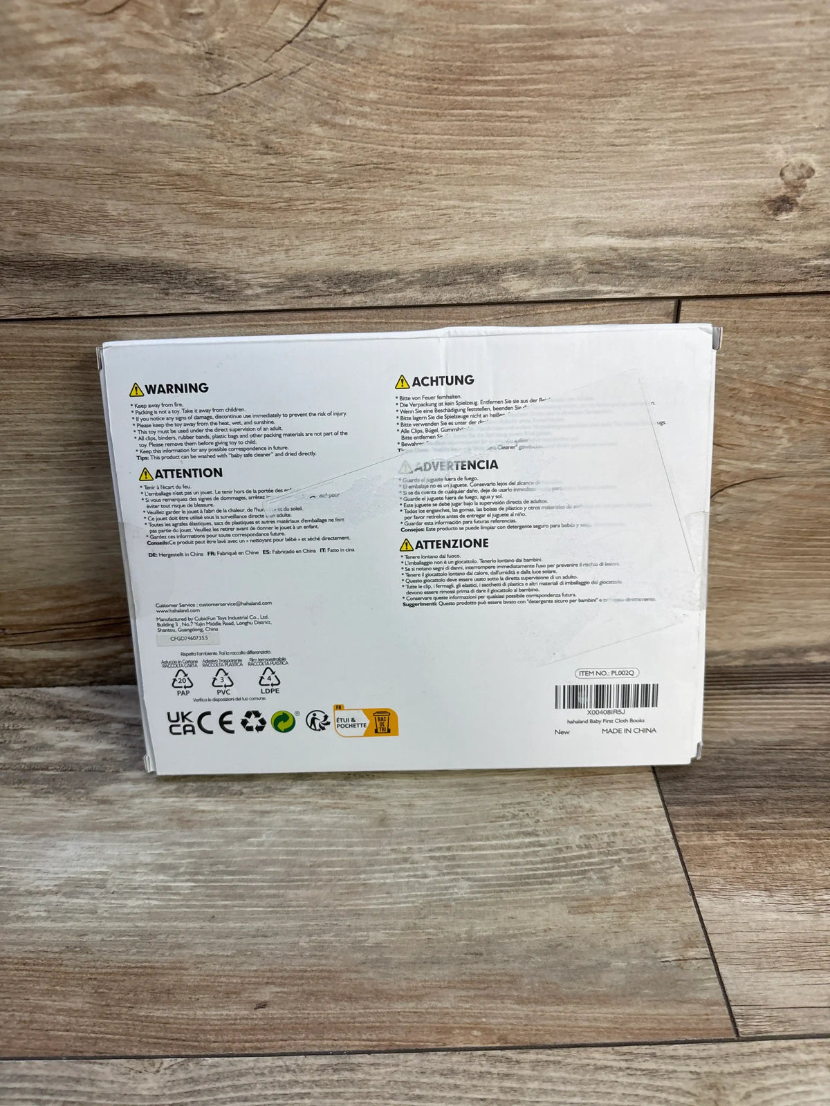 Rear view of HahaLand two-pack baby first cloth books packaging showing multilingual safety warnings on a wood floor