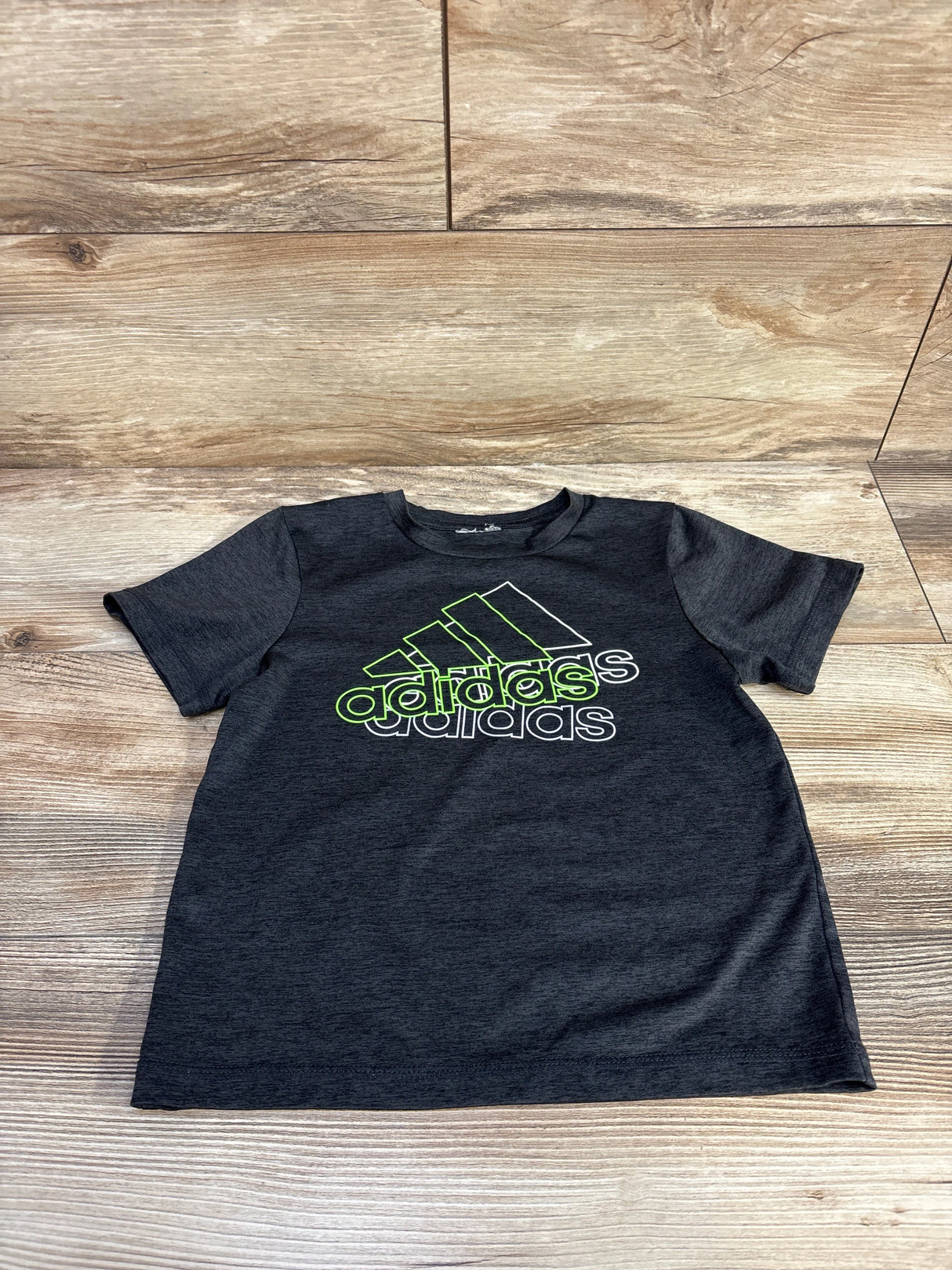 Dark gray Adidas kids t-shirt with neon green and white logo on wood floor