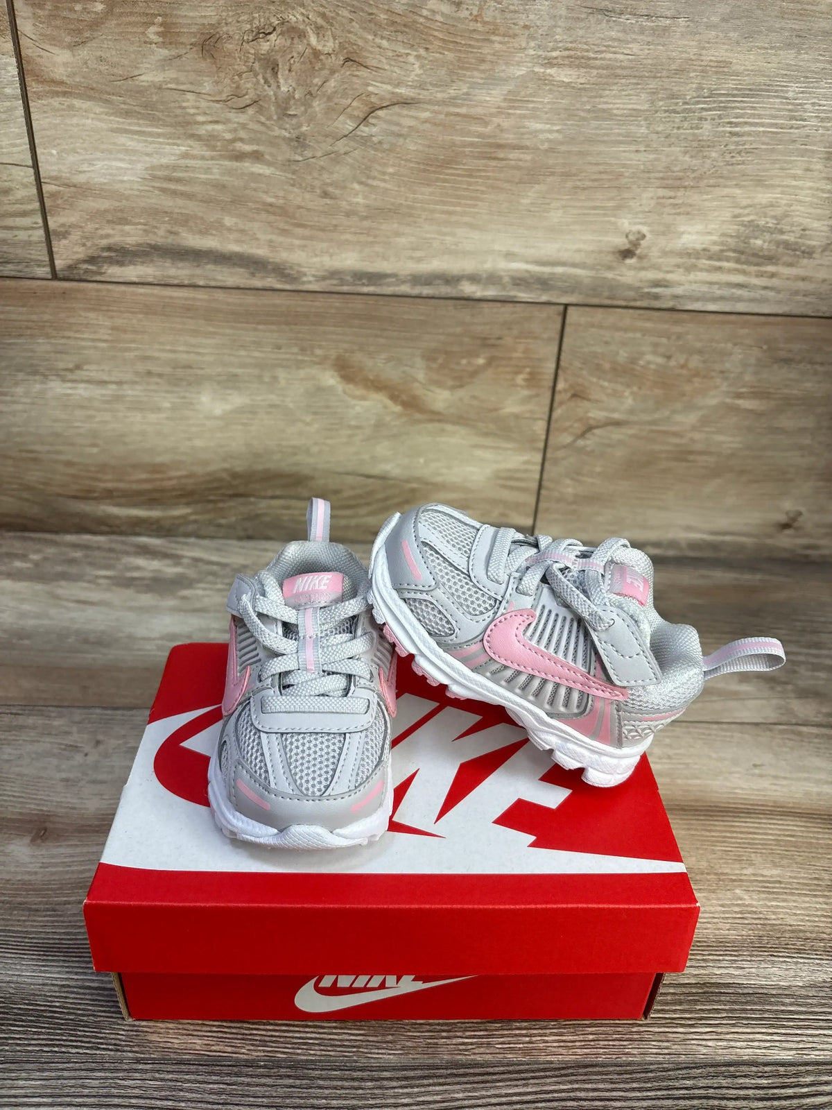 Front and side view of Nike Vomero 5 TD toddler sneakers in grey and pink showcasing mesh upper, velcro strap, and white sole on red Nike box