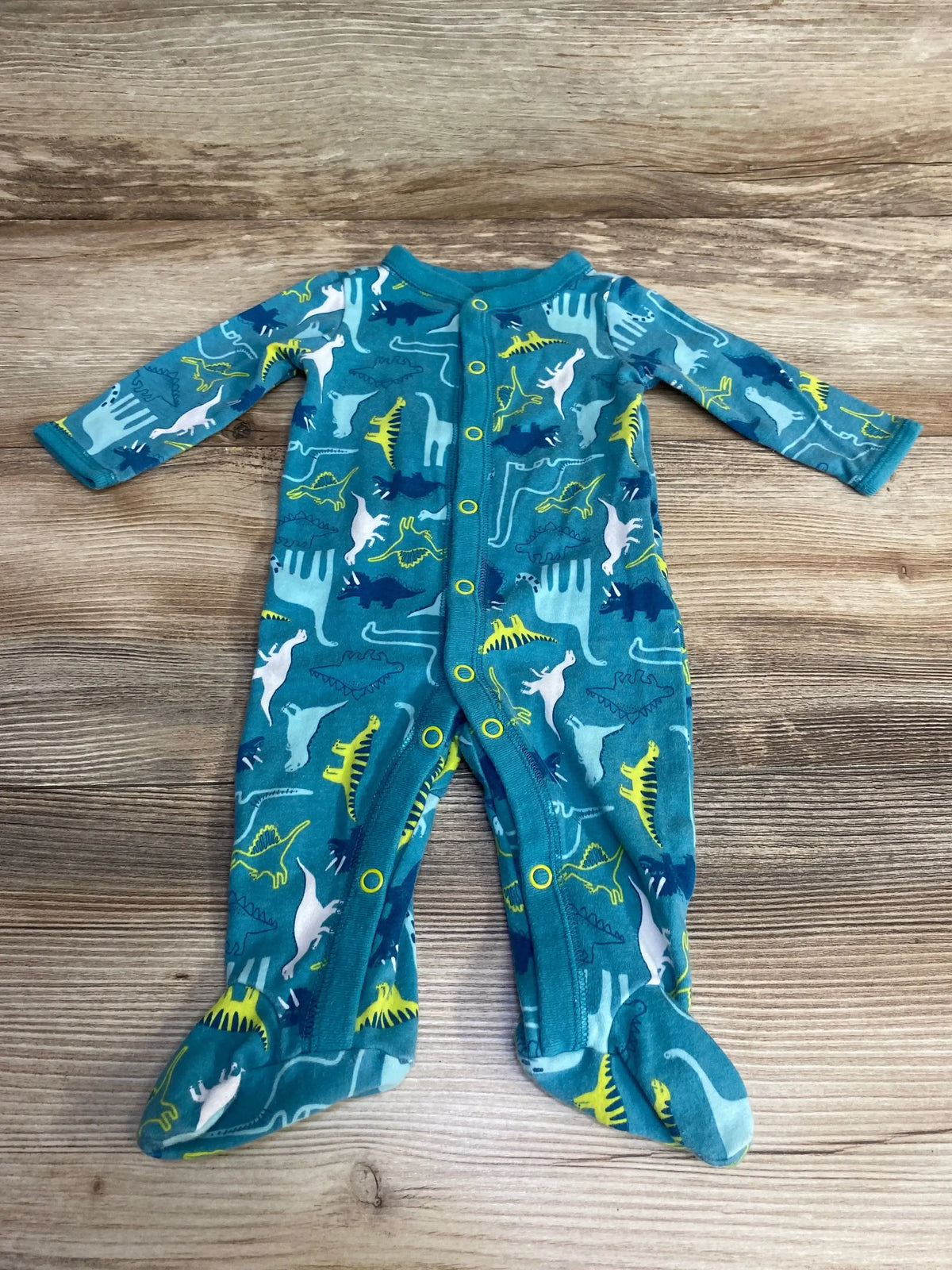 Flat lay of Carter’s blue footed sleeper showing multicolor dinosaur print, front snap closure on wood background