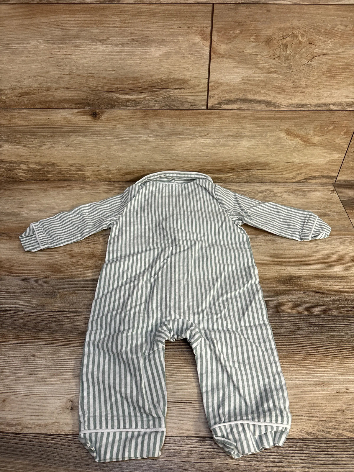 Flat lay view of a green and white striped button up coverall showcasing long sleeves and full length legs on a wood surface