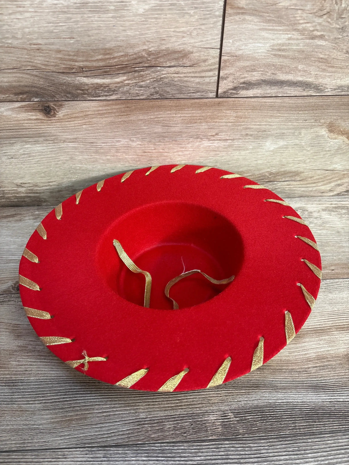 Red felt sombrero with gold trim, kids party hat on wooden floor