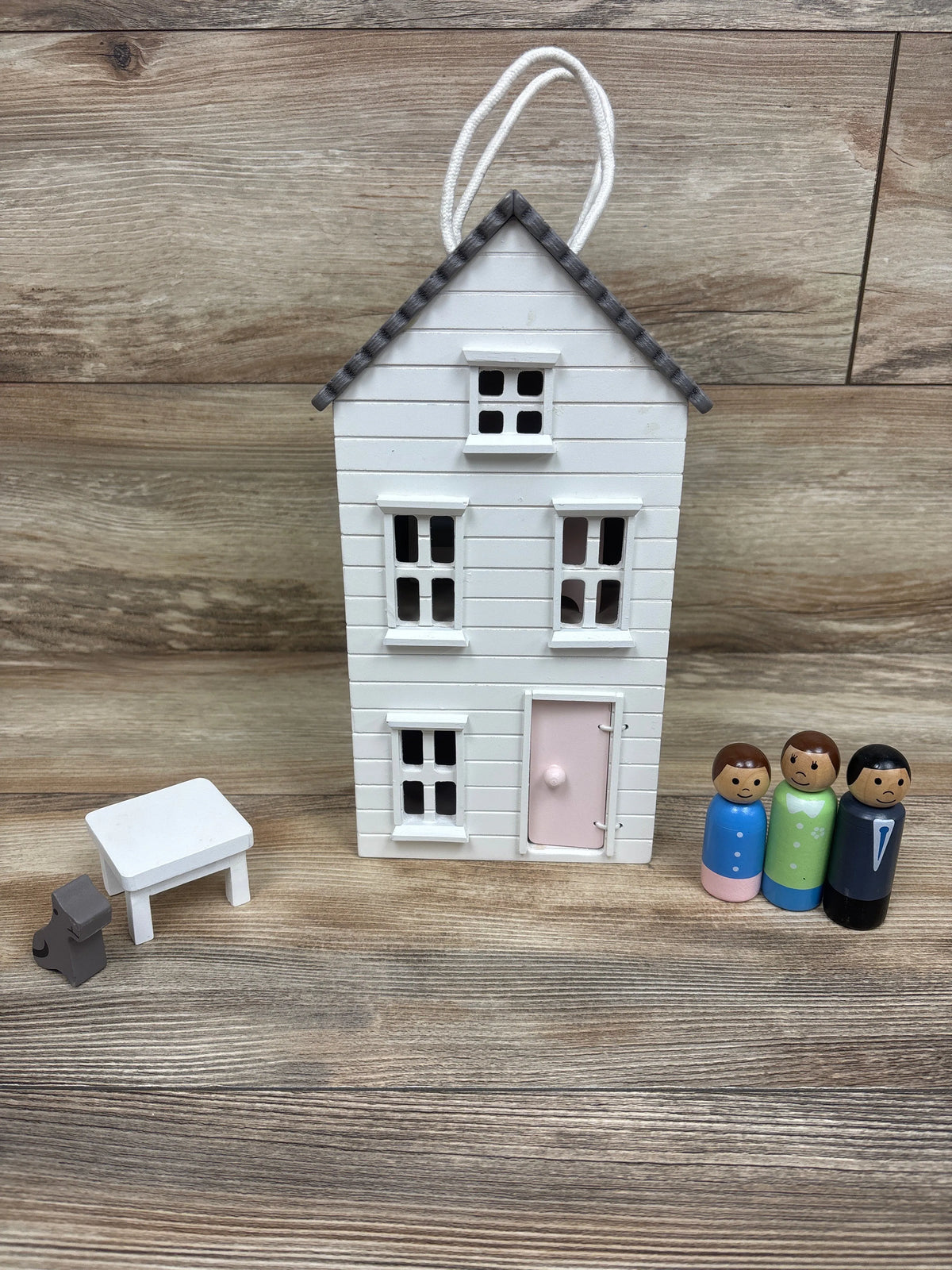 Front view of Pottery Barn Kids Take-Along wooden dollhouse with white siding, pink door, three dolls, table, and dog