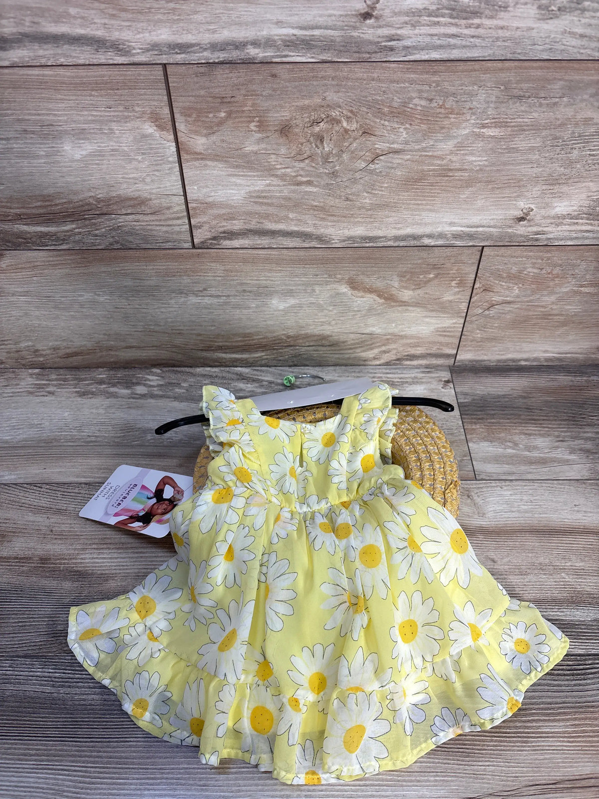 Flat lay of Blueberi Boulevard yellow floral dress and straw sun hat set on a wood floor
